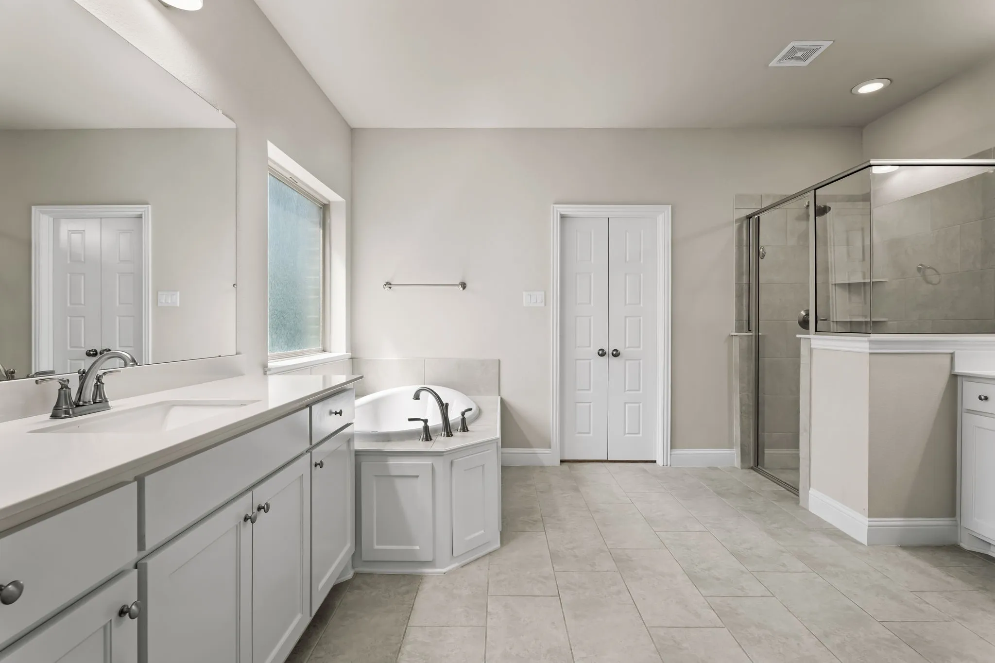 Contemporary bathroom featuring a large soaking tub, glass-enclosed shower, dual vanity with white cabinetry, and tiled flooring