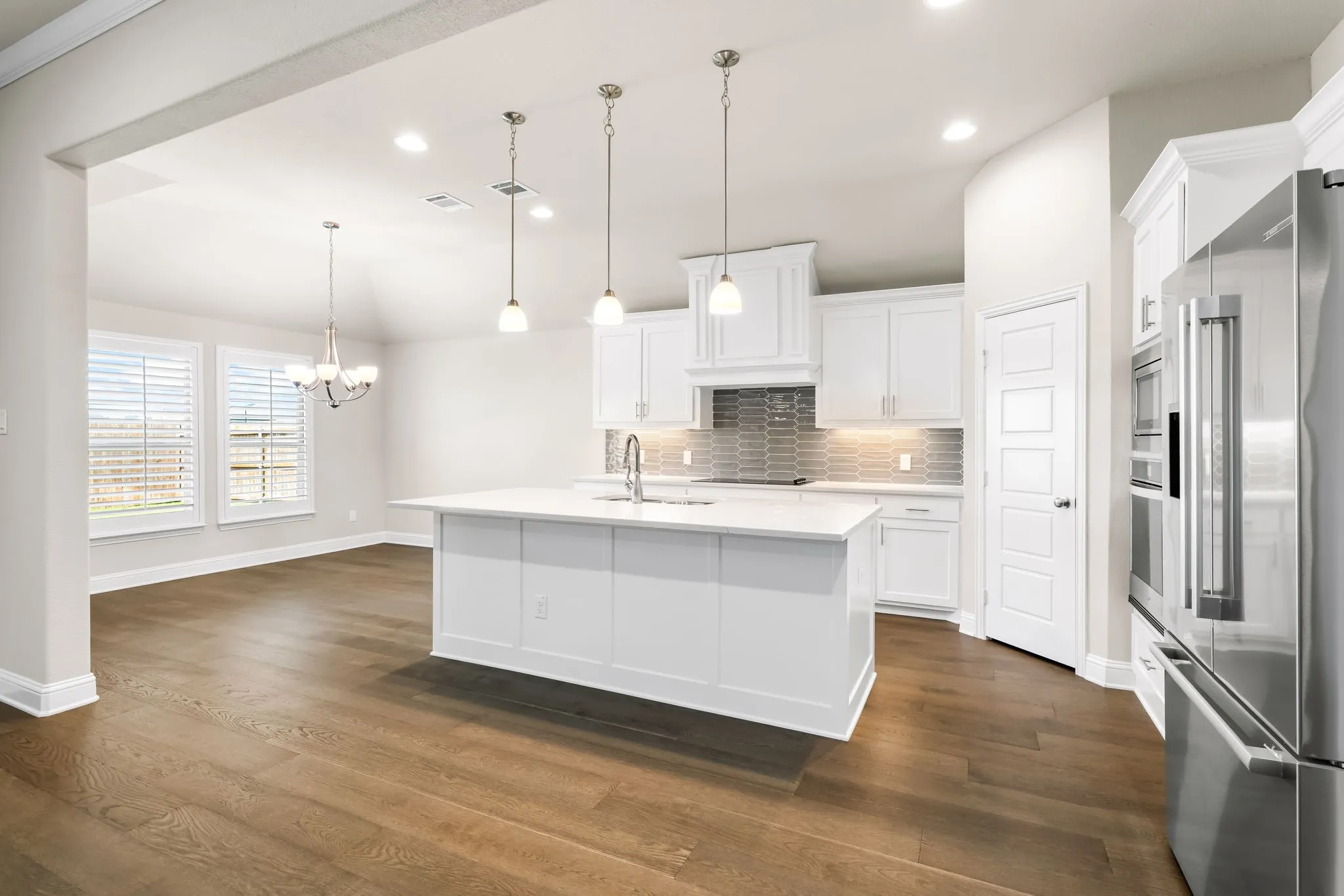 Open-concept kitchen featuring a central island, white cabinetry, stainless steel appliances, and wood-finish flooring