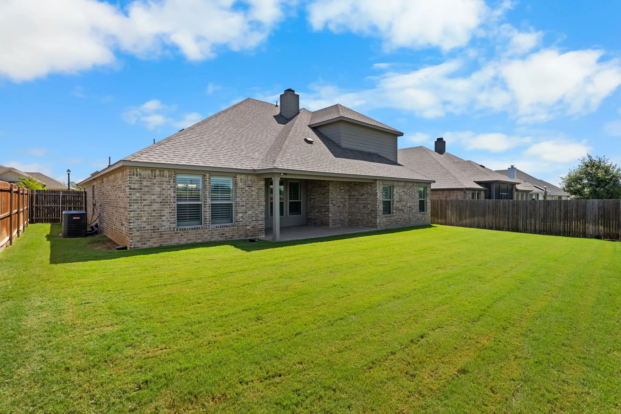 Expansive rear yard featuring a covered patio, brick exterior, and a privacy fence