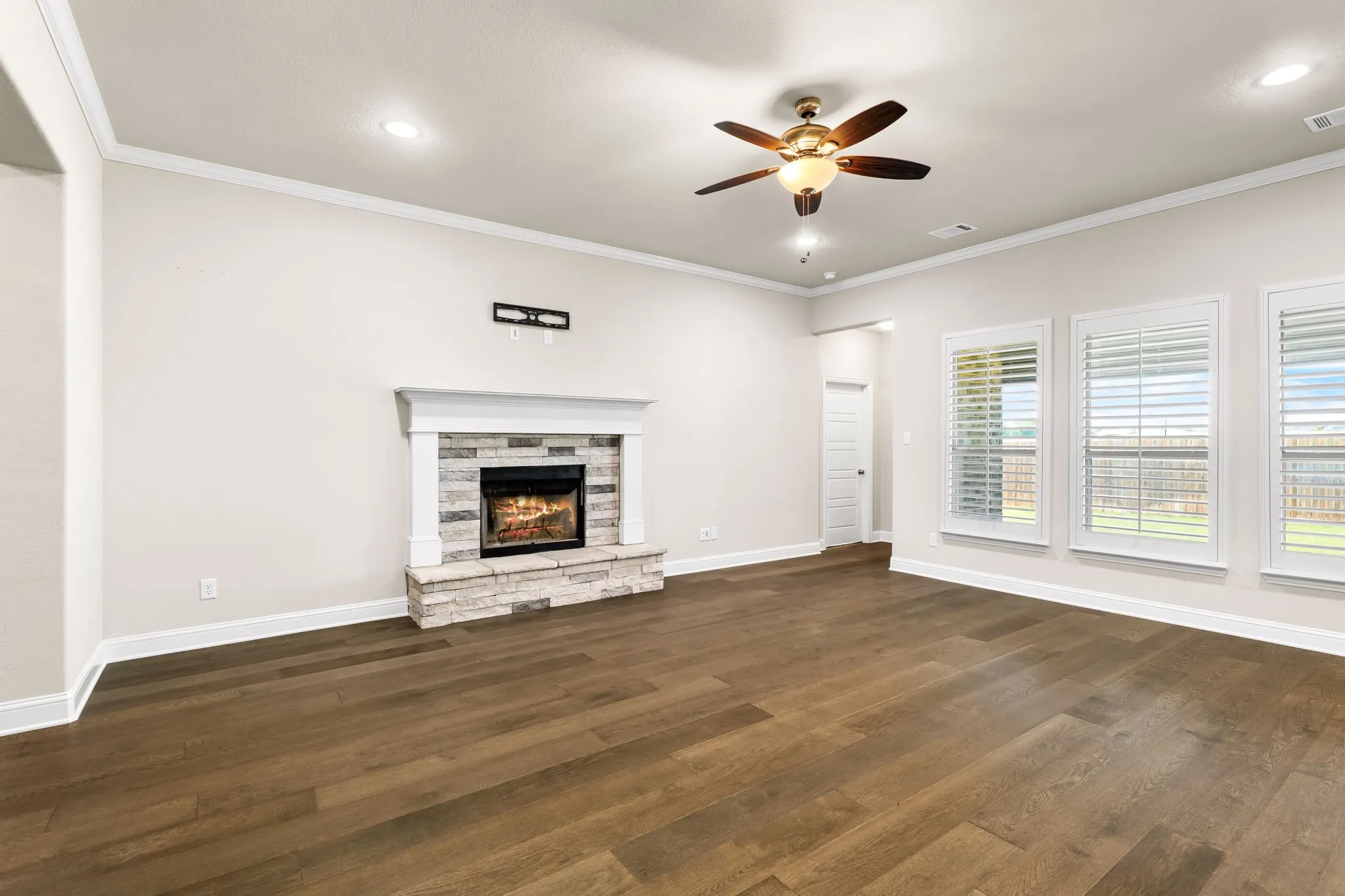 Spacious room featuring wood-finish flooring, a stone-surround fireplace with mantel, crown molding, and recessed lighting