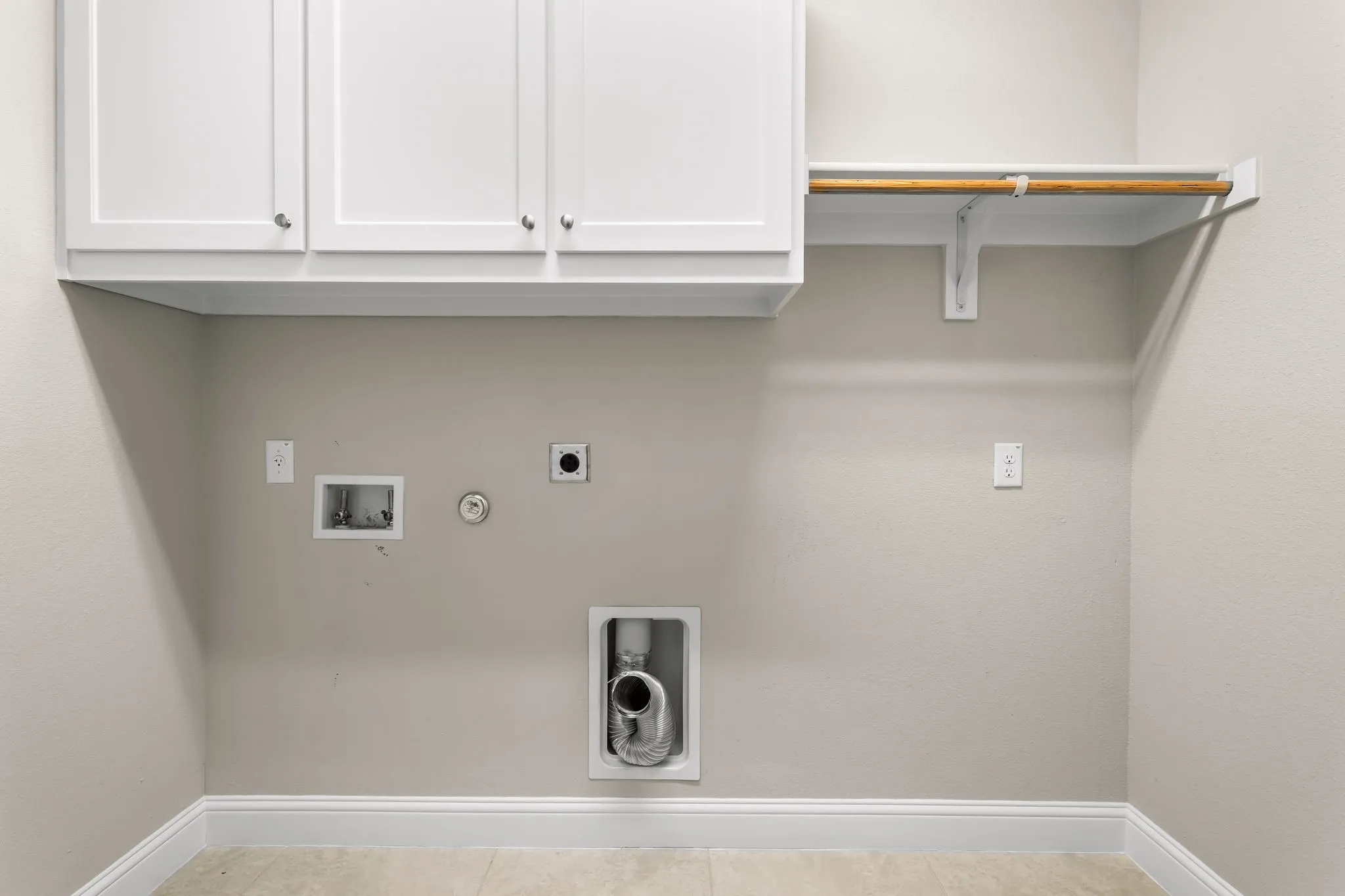 Laundry area featuring white shaker-style cabinetry, a built-in hanging rod with shelving, neutral wall paint, and tile flooring