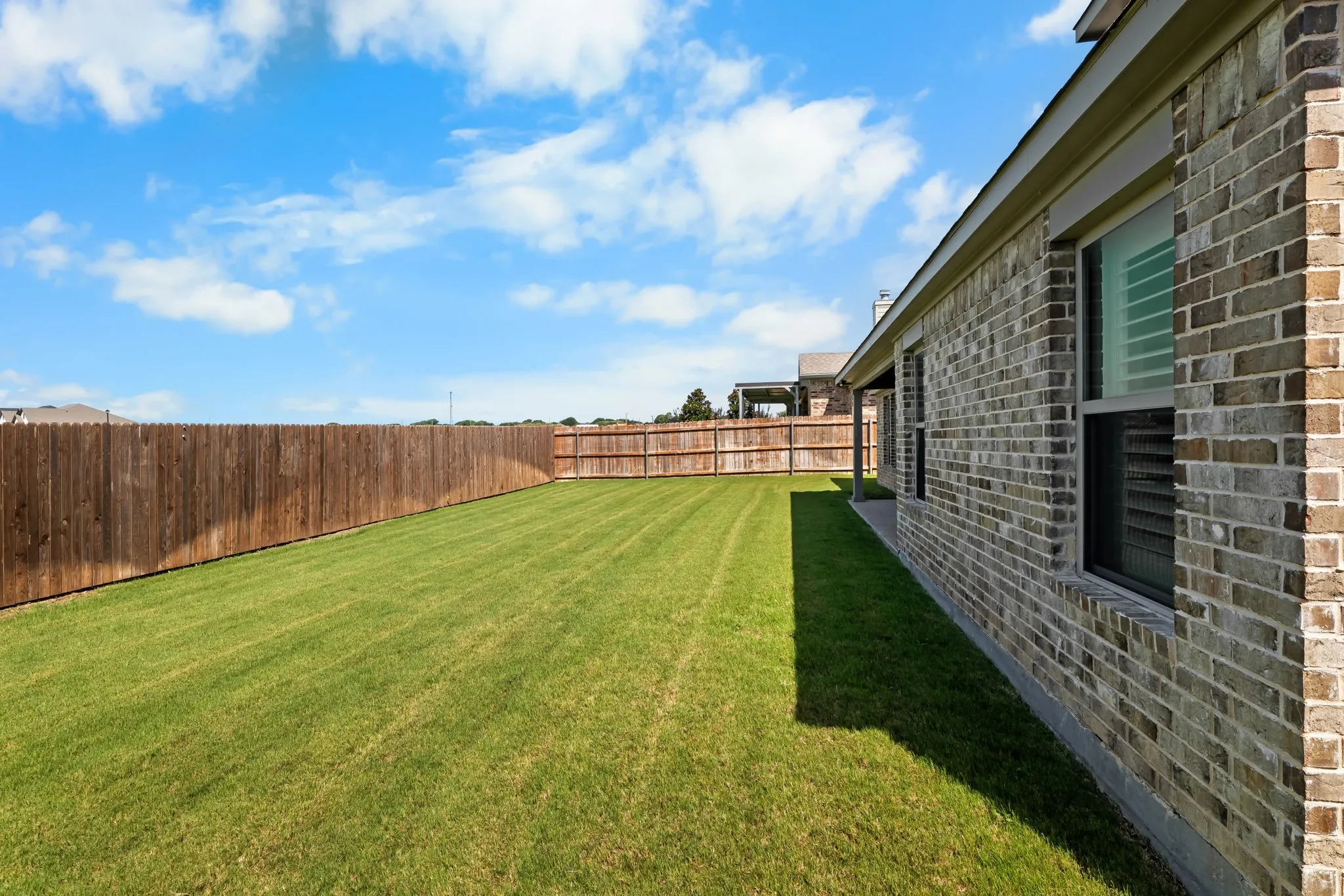 Expansive backyard featuring a manicured lawn, full privacy fencing, and a brick exterior with multiple windows