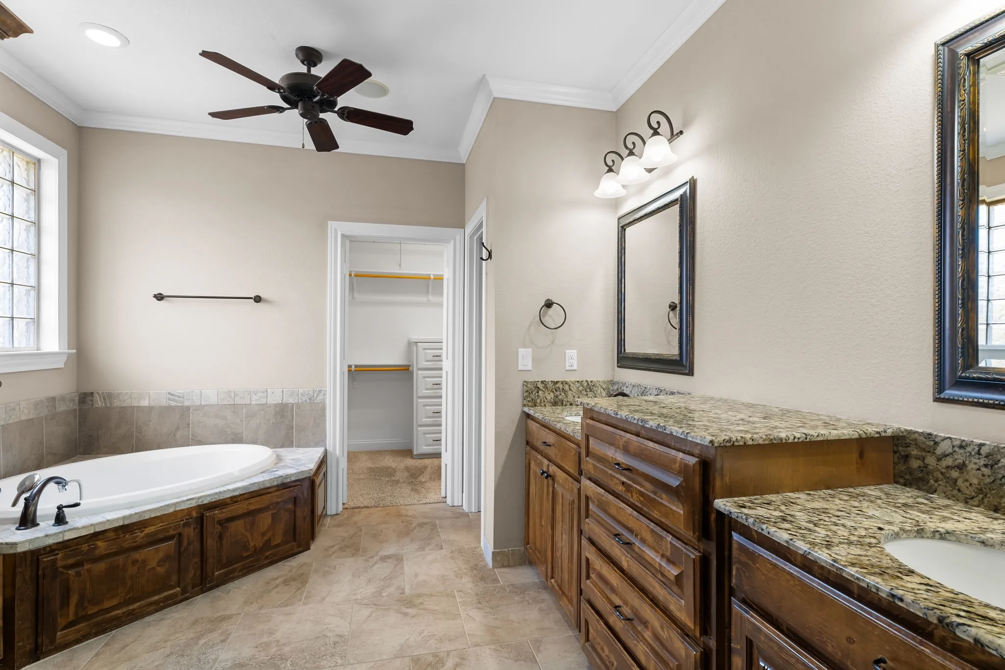 Bathroom featuring a built-in soaking tub with stone tile surround, dual vanities with granite countertops and wood cabinetry, and tiled flooring