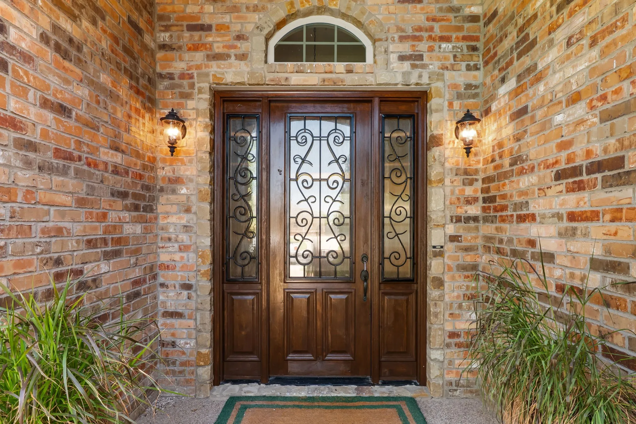 Brick exterior featuring a wood-panel entry door with decorative ironwork, glass sidelights, and an arched transom window
