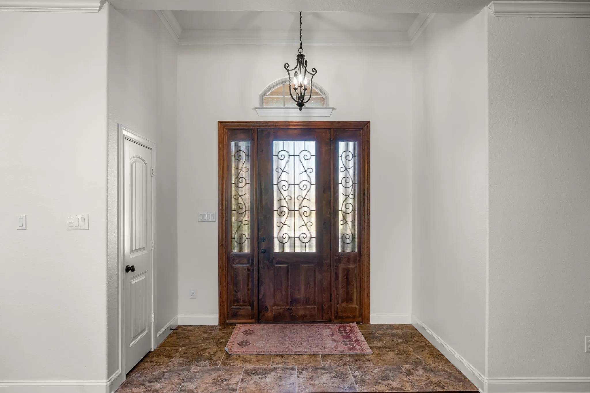 Entryway featuring a dark wood door with decorative glass inserts and sidelights, an arched transom window, and a wrought iron​​‌​​​​‌​​‌‌​‌‌​​​‌‌​‌​‌​‌​​​‌​​ chandelier