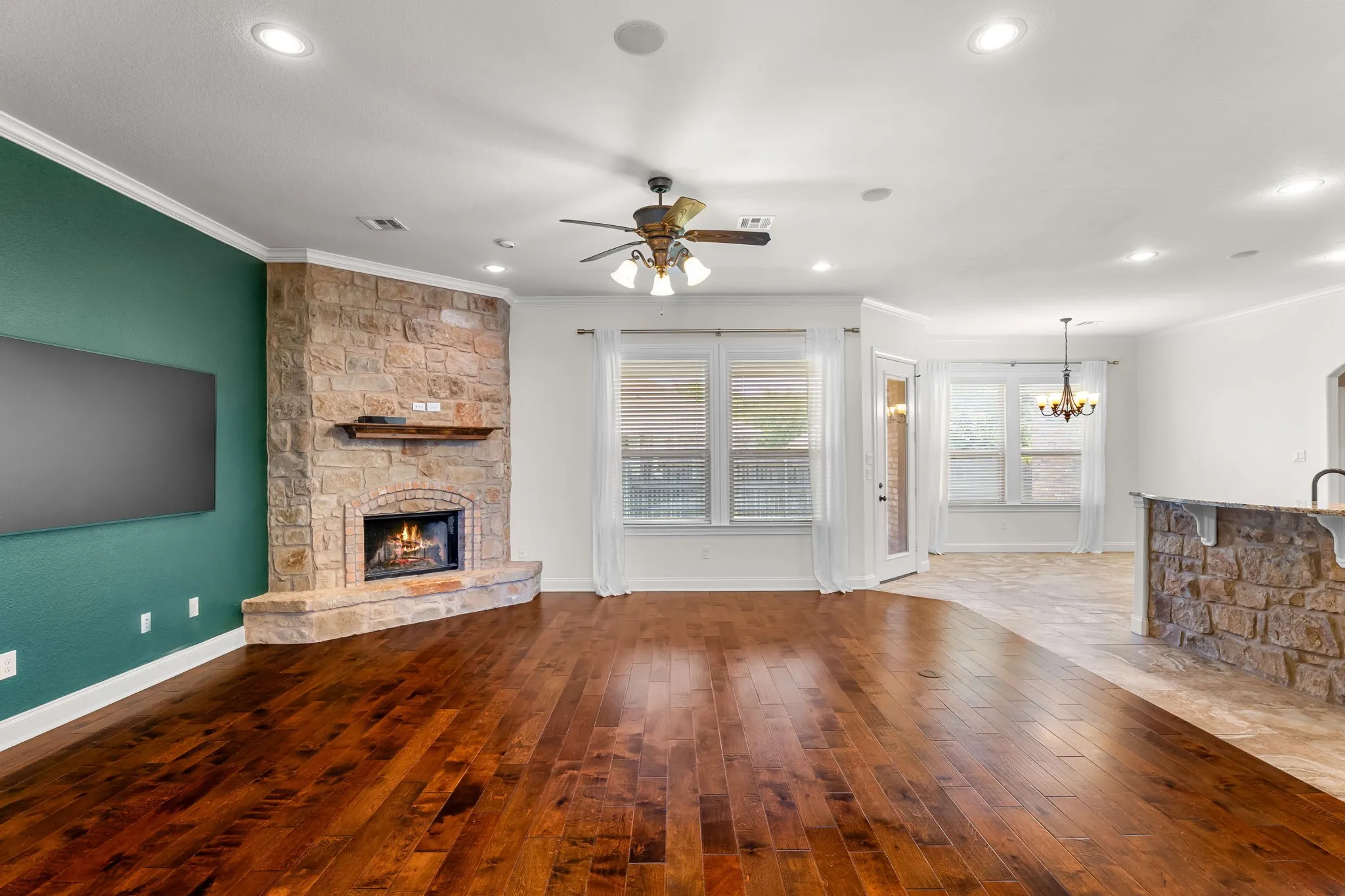 Spacious living area featuring rich wood-finish flooring, a stone-clad corner fireplace with a mantel, and recessed lighting