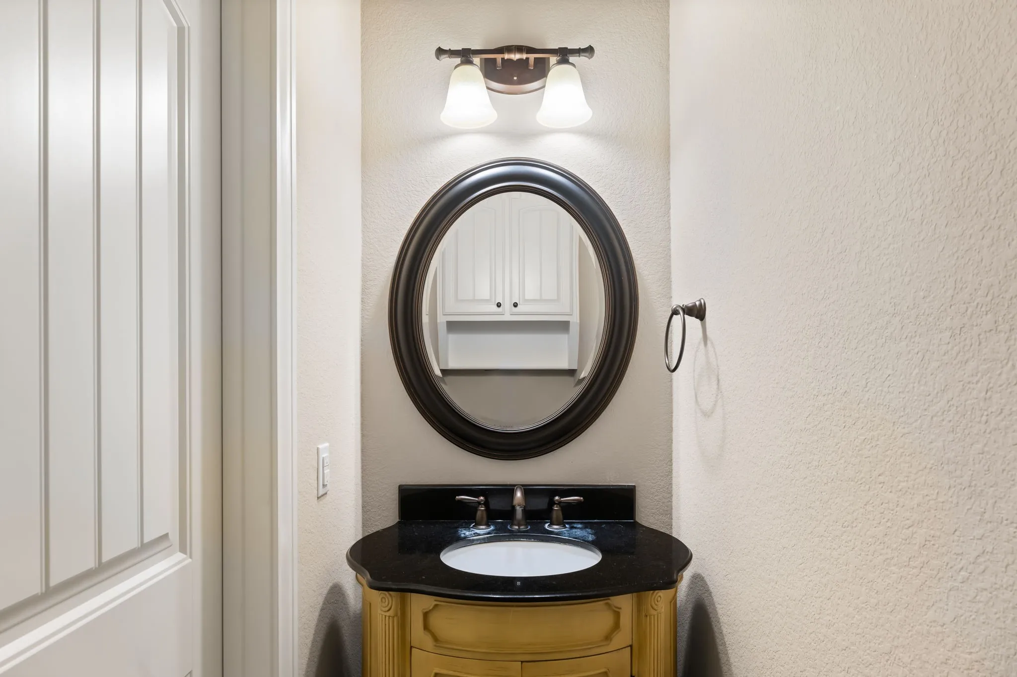 Powder room featuring a decorative wood vanity with a black countertop, oval undermount sink, and a bronze-finish faucet