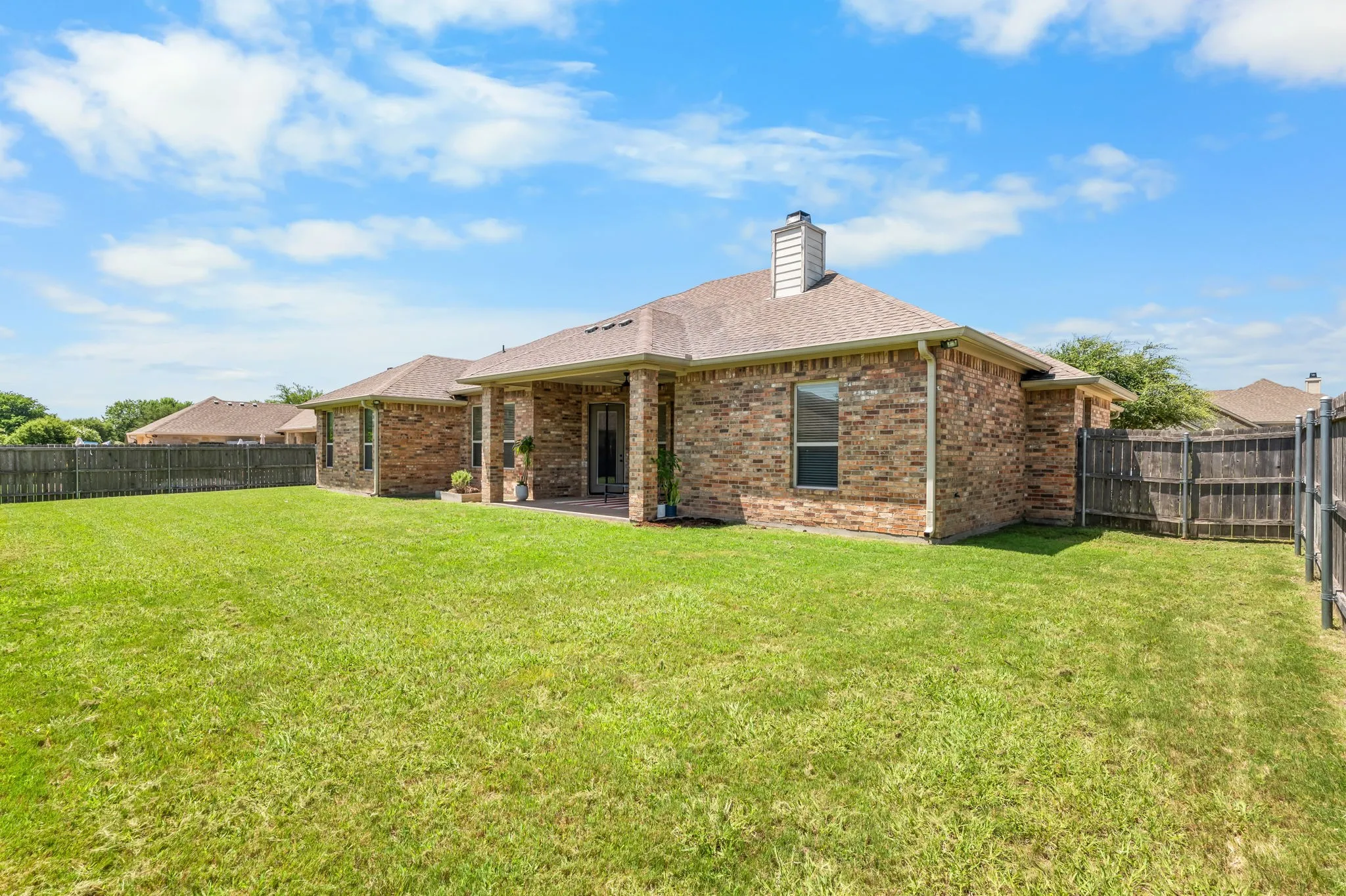 Expansive backyard with a manicured lawn, full privacy fencing, and a covered patio area