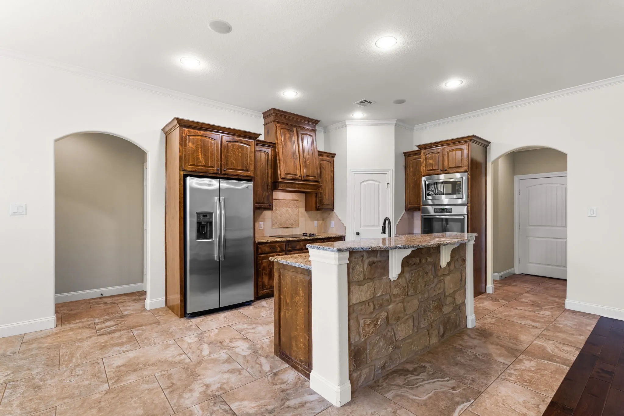 Kitchen featuring a stone-faced island with granite countertop, stainless steel appliances, dark wood cabinetry, and recessed lighting