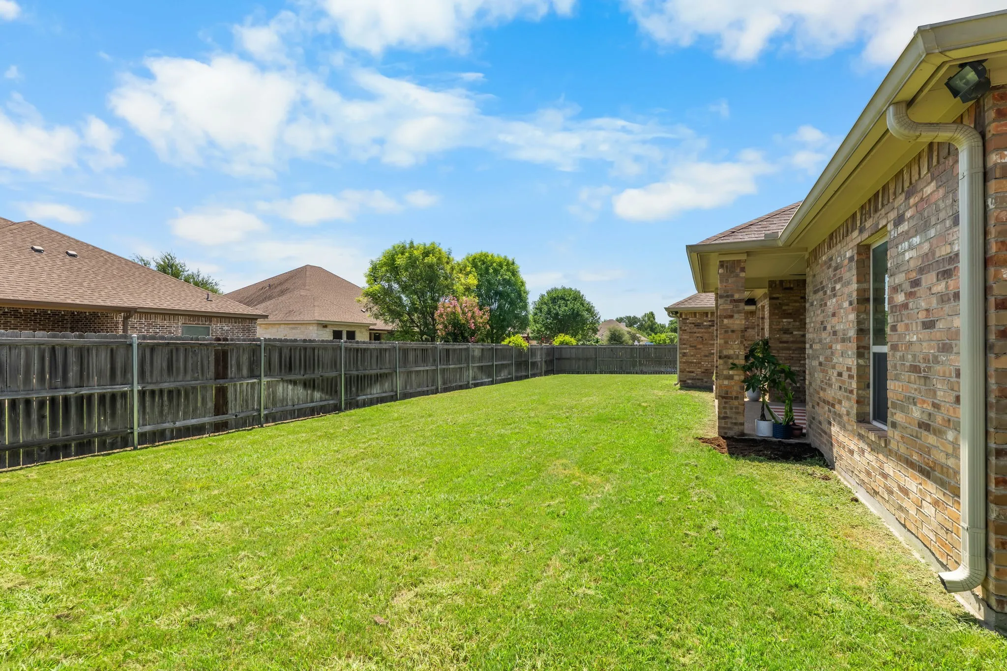 Expansive backyard featuring a lush green lawn, full privacy fencing, and brick exterior