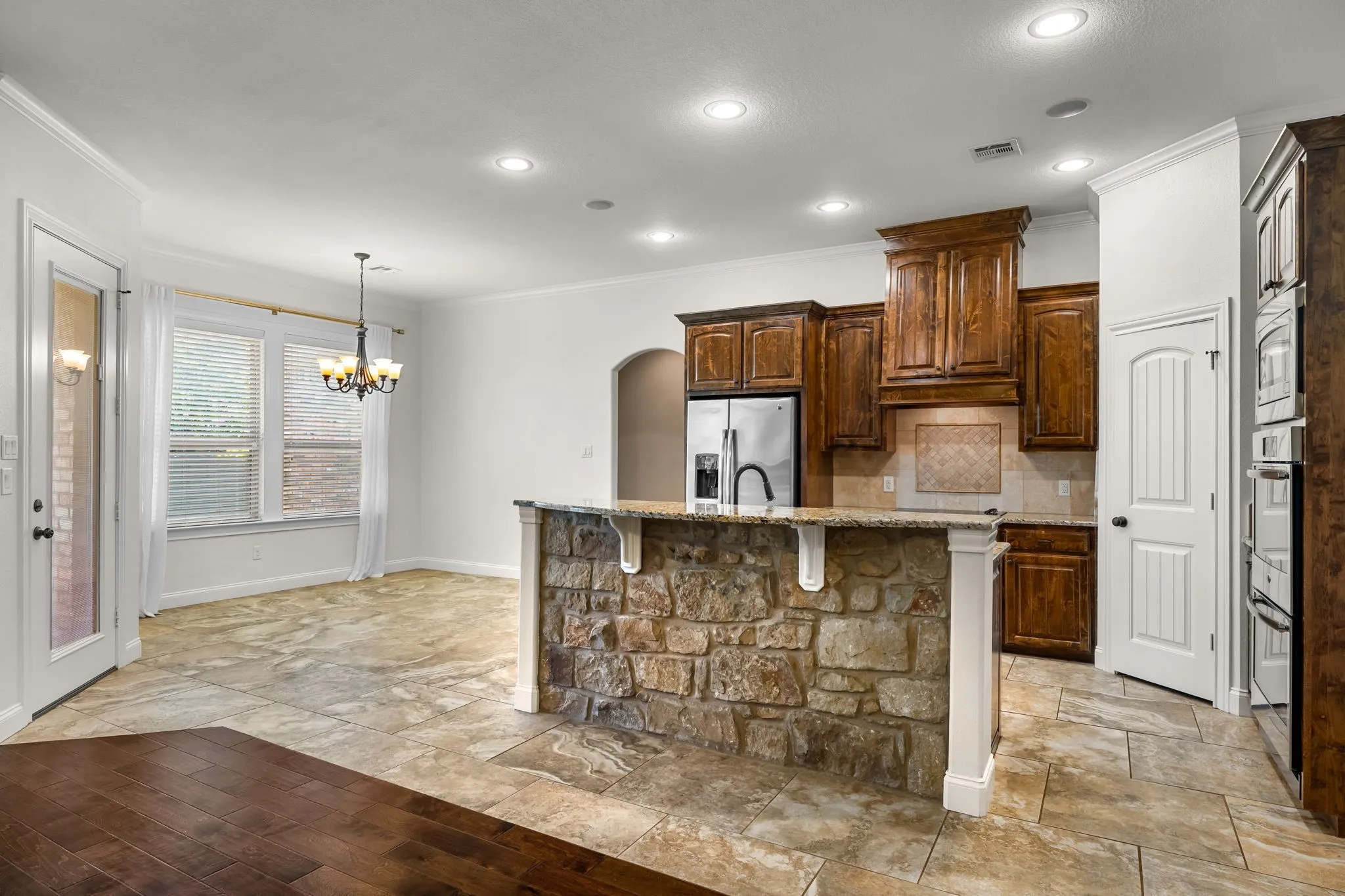 Kitchen featuring a stone-clad island with a granite countertop, wood cabinetry, stainless steel appliances, and recessed lighting