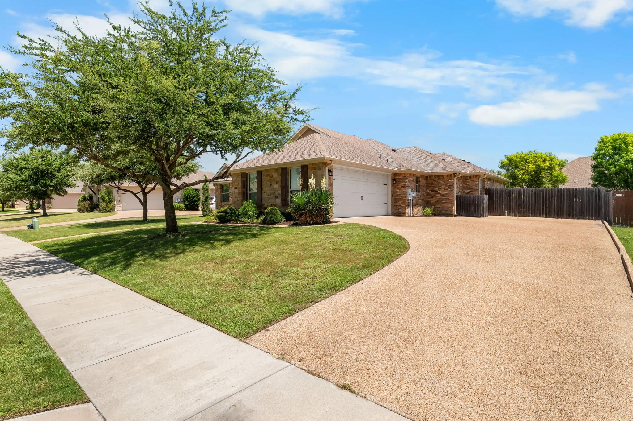 Brick exterior residence featuring an exposed aggregate driveway, an attached two-car garage, and a manicured lawn