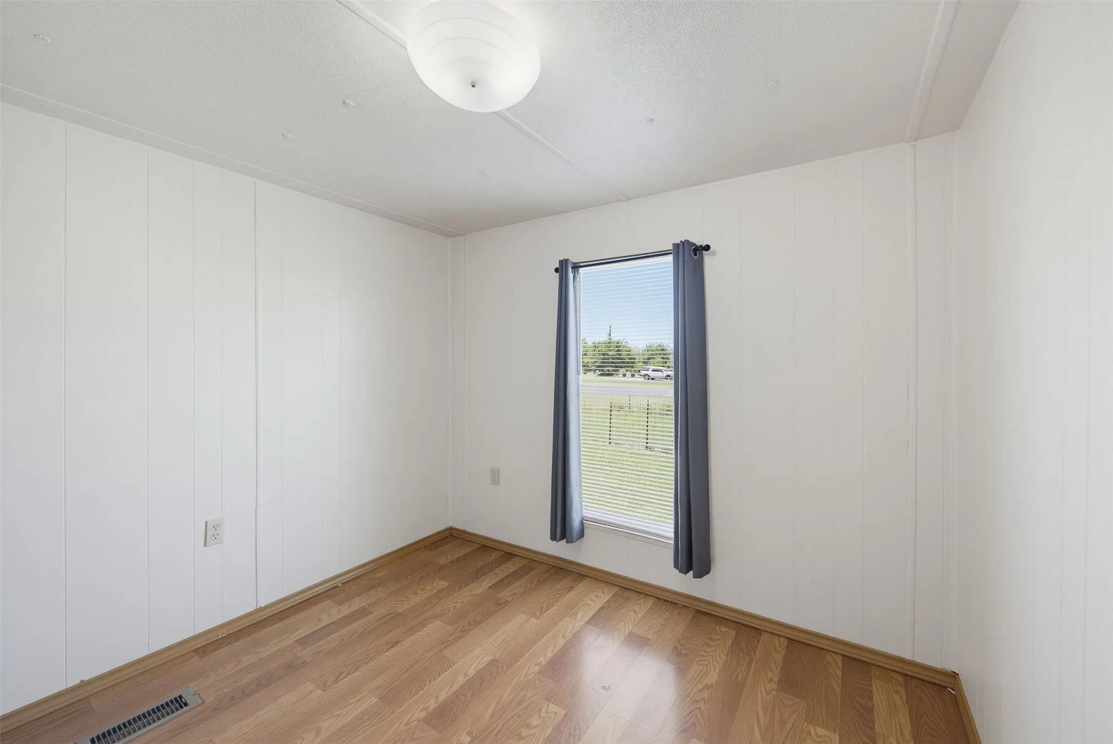 Room featuring wood-finish flooring, white vertical paneled walls, and a window with blinds