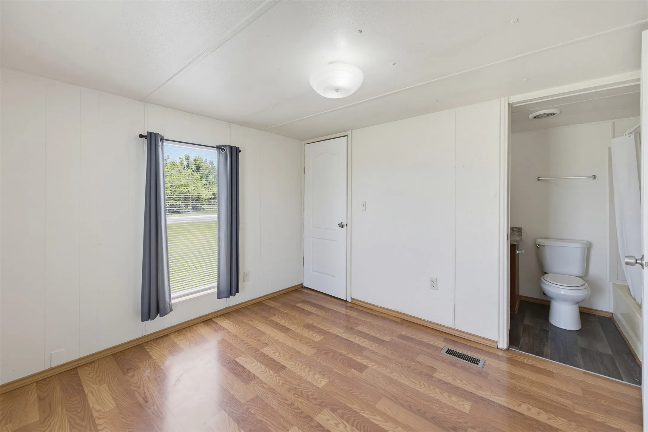 Spacious interior room featuring wood-finish flooring and a white paneled wall finish