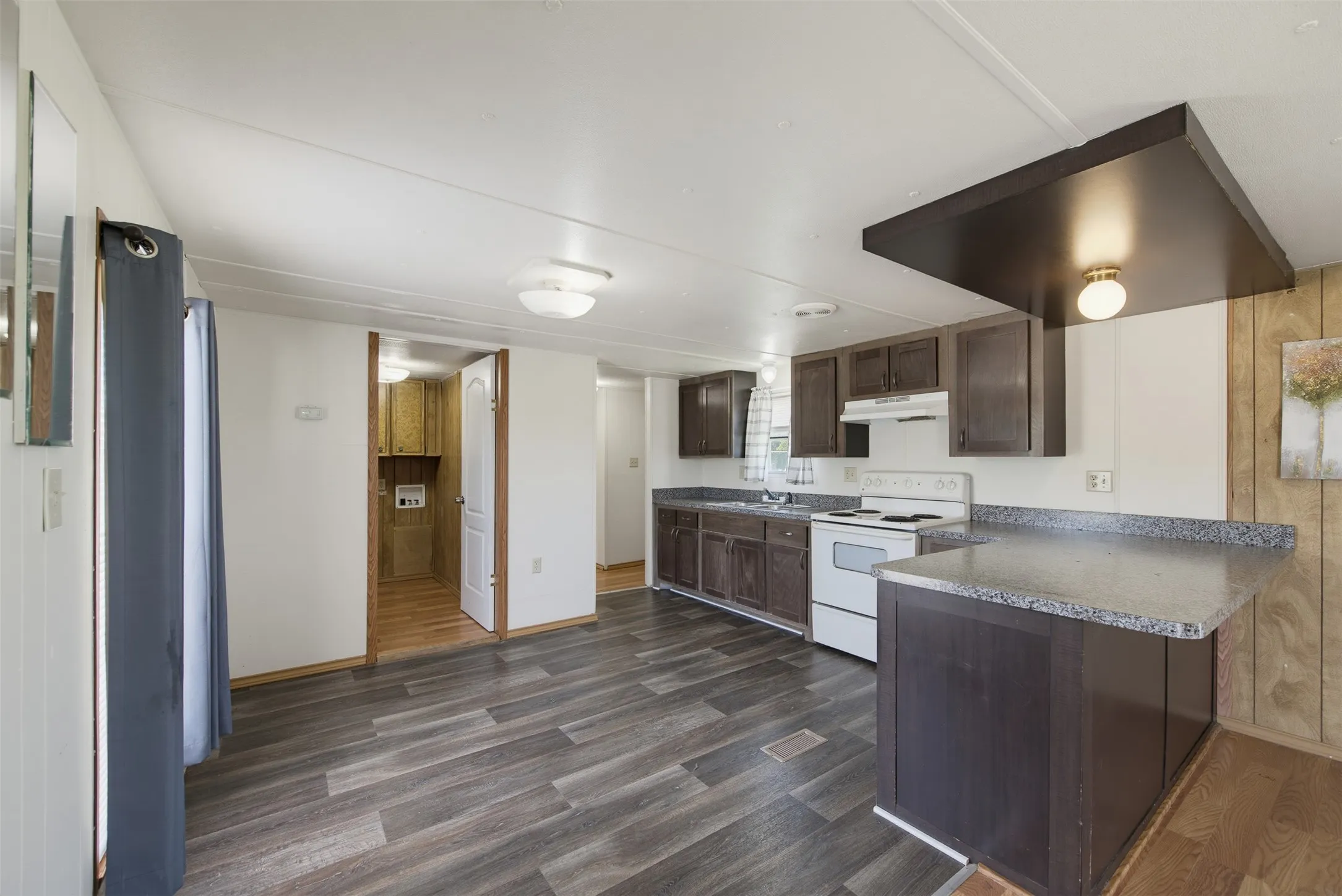 Kitchen featuring dark wood-finish cabinetry, white appliances, and a breakfast bar with a speckled countertop
