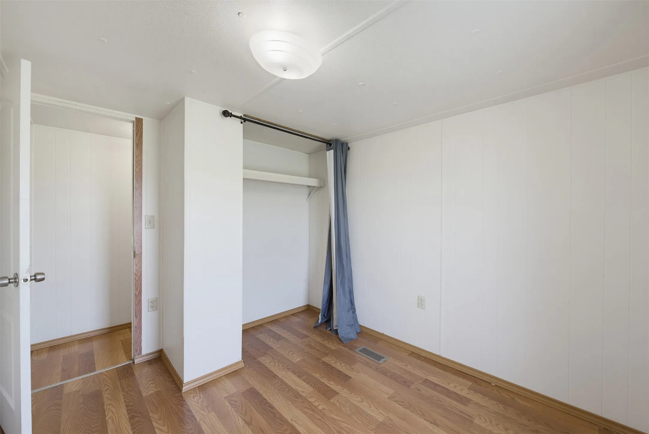 Interior room featuring wood-finish flooring, white paneled walls, and a ceiling-mounted light fixture