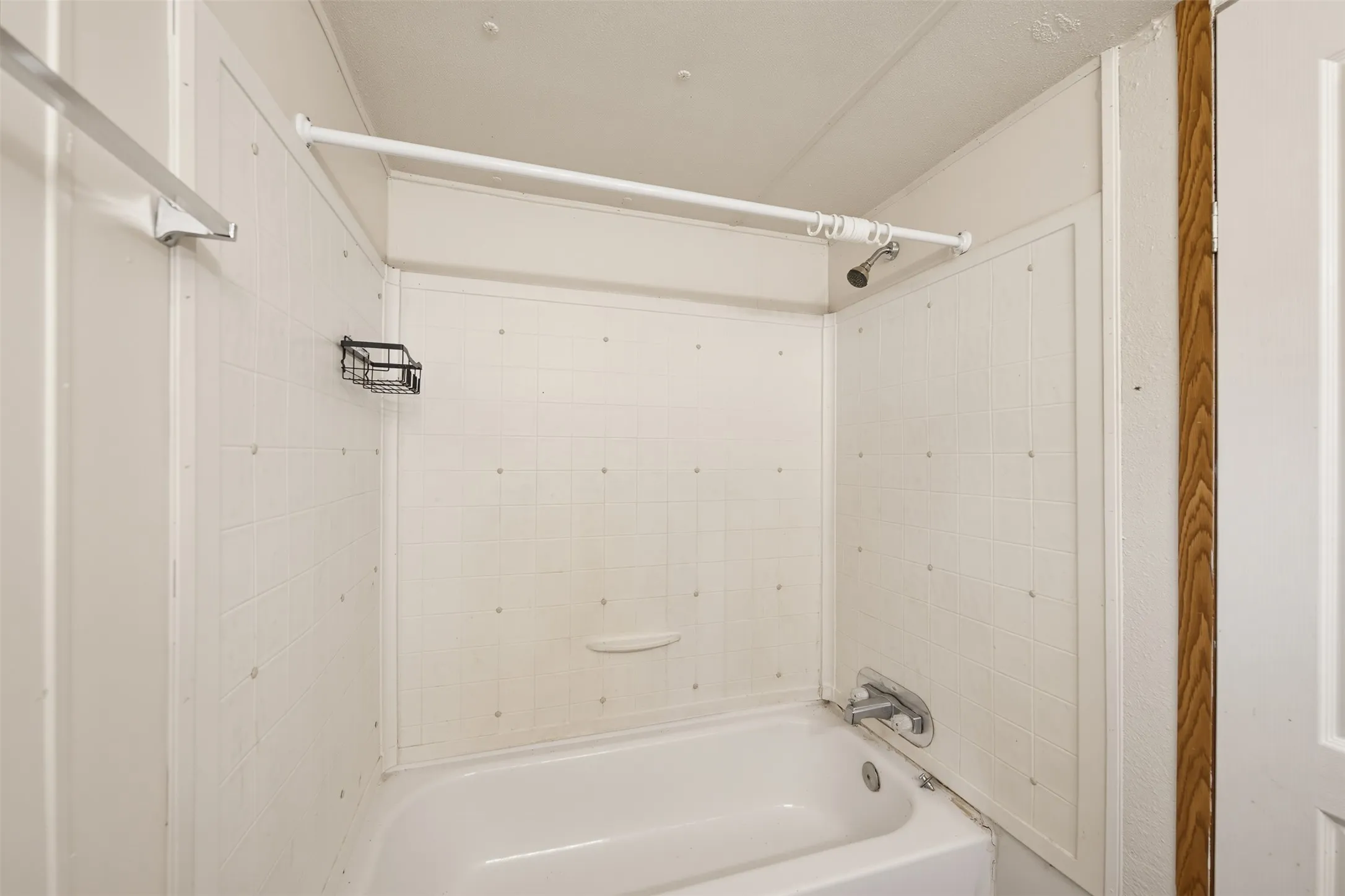 White bathtub with integrated shower, white shower surround, and chrome fixtures