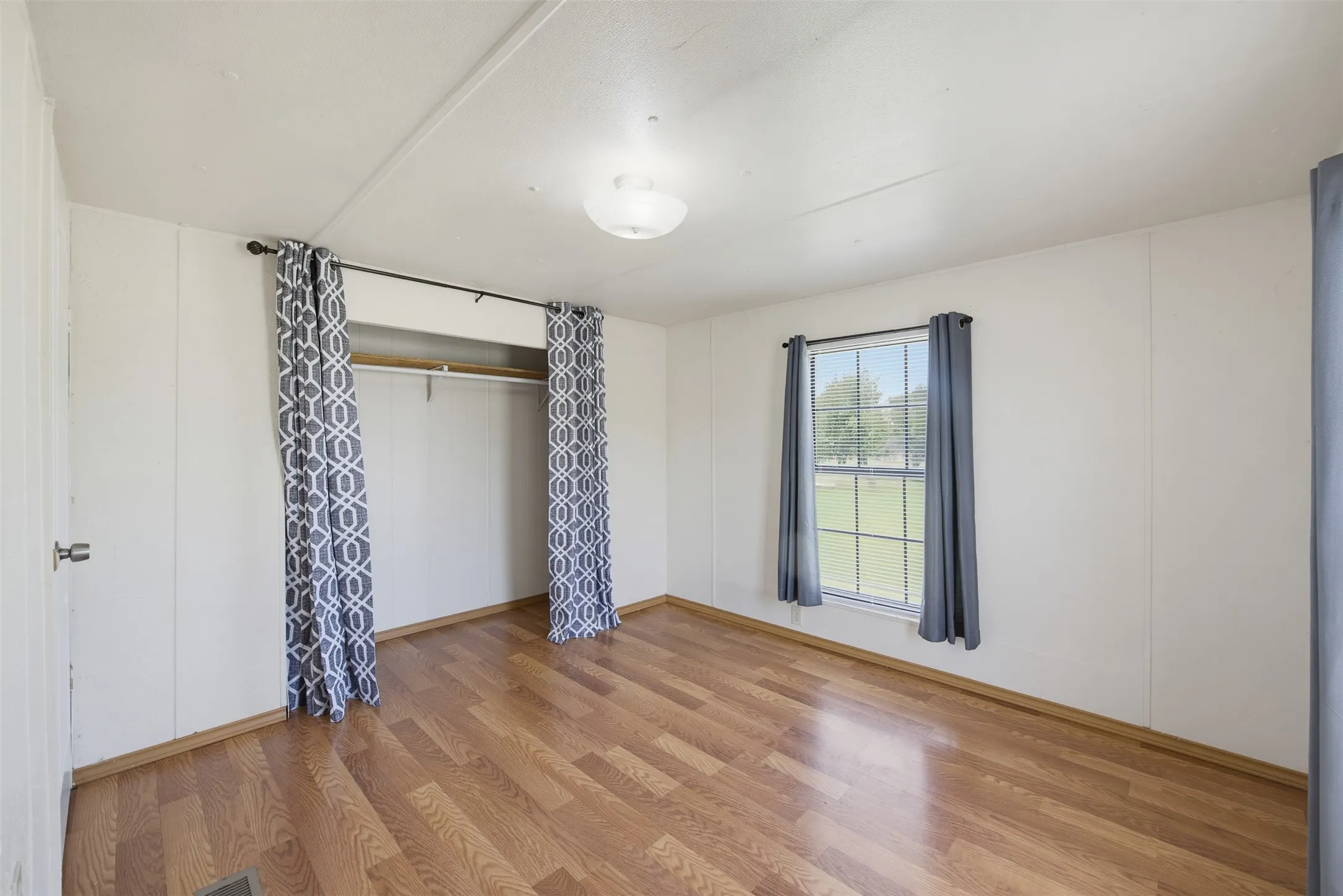 Interior room featuring wood-finish flooring, white panel walls, and a window with a green exterior landscape