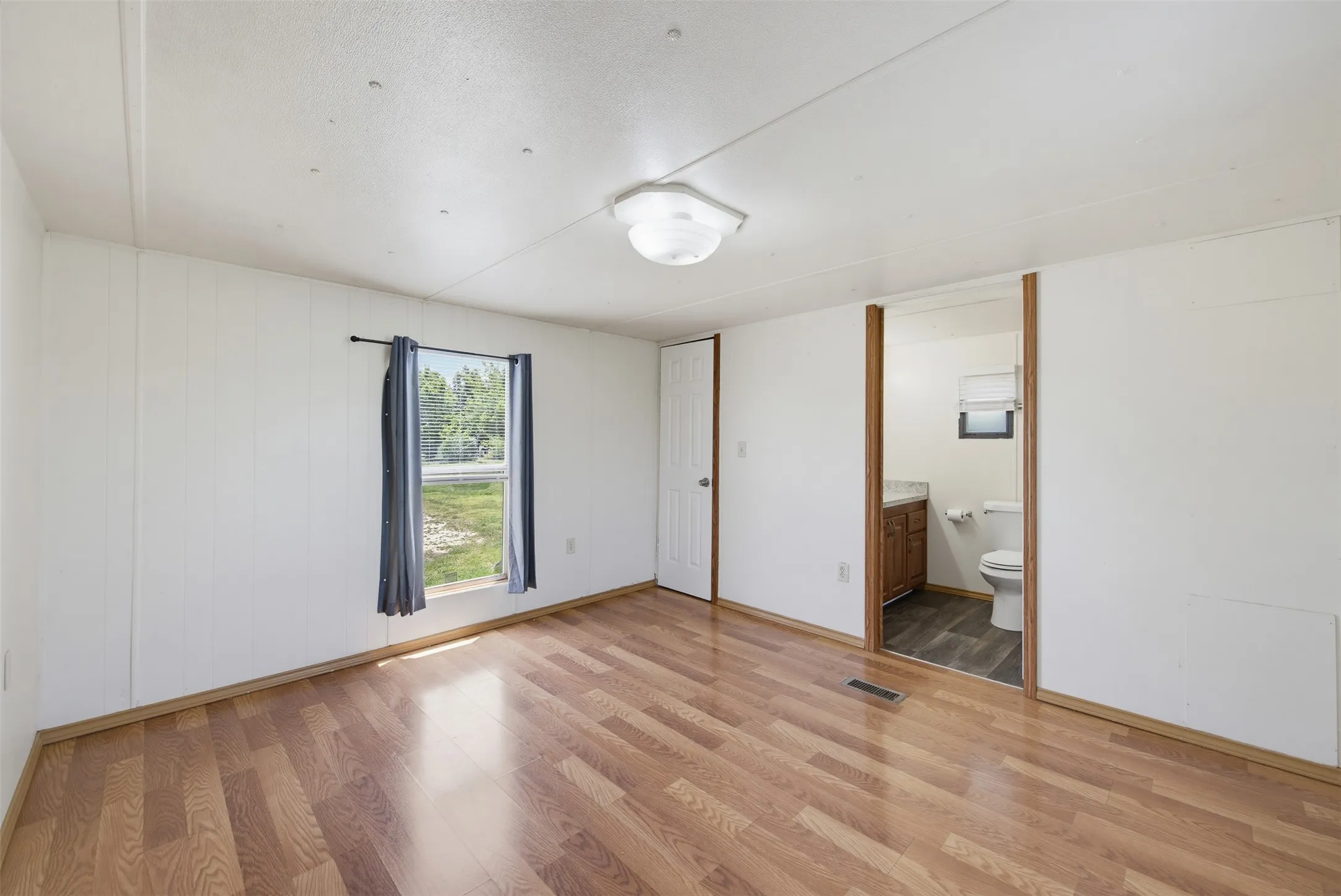 Spacious room featuring wood-finish flooring, white panel walls, and a ceiling-mounted light fixture