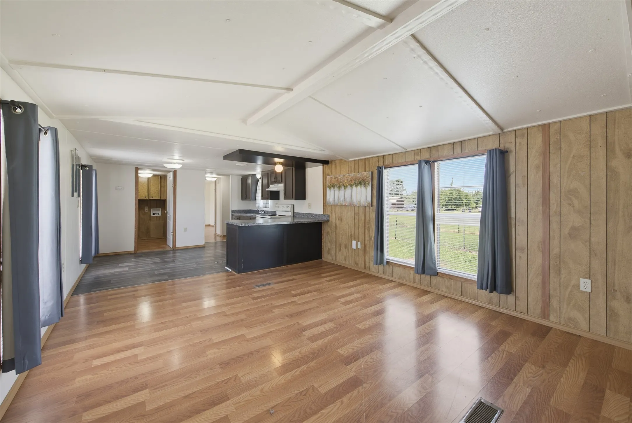 Open-concept living space featuring wood-finish flooring, paneled accent wall, and multiple windows