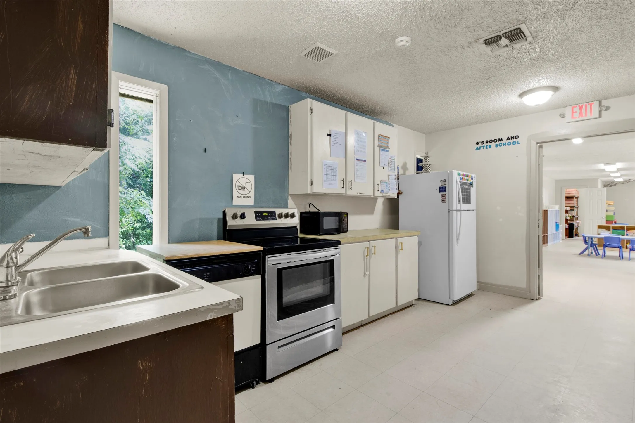 Functional kitchen space featuring a dual basin stainless steel sink, white cabinetry, a freestanding range, and a refrigerator