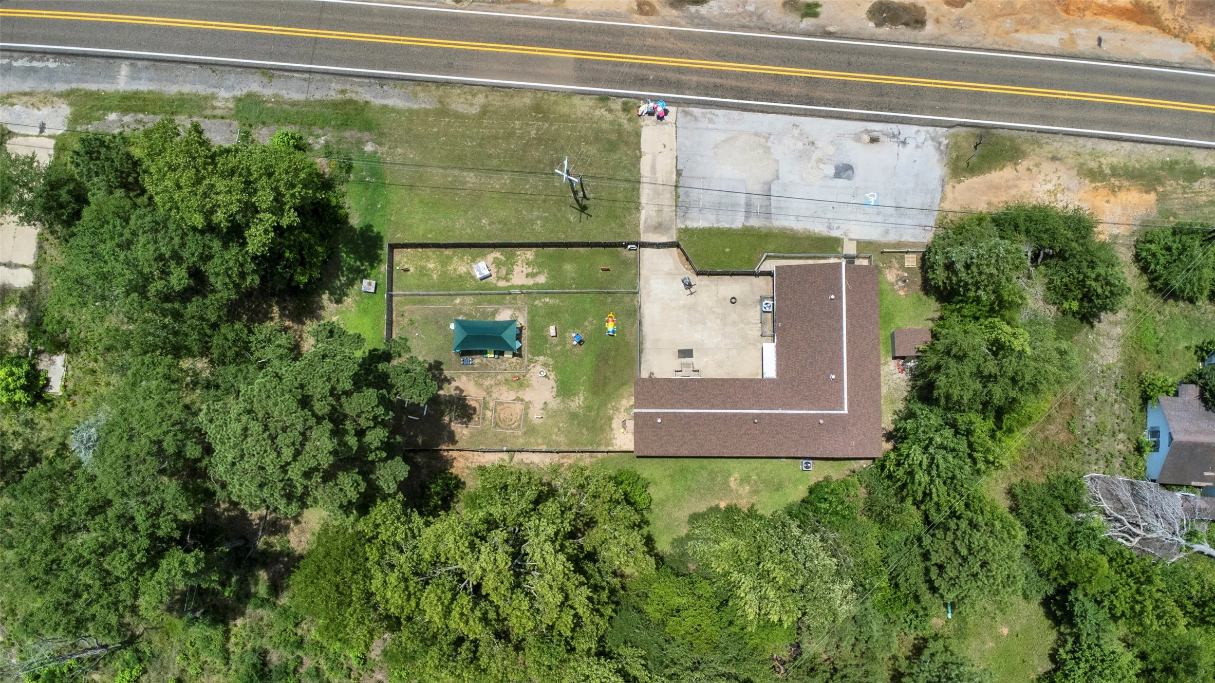 Expansive property featuring a large L-shaped building with a brown shingle roof, a separate green-roofed structure, and a concrete patio
