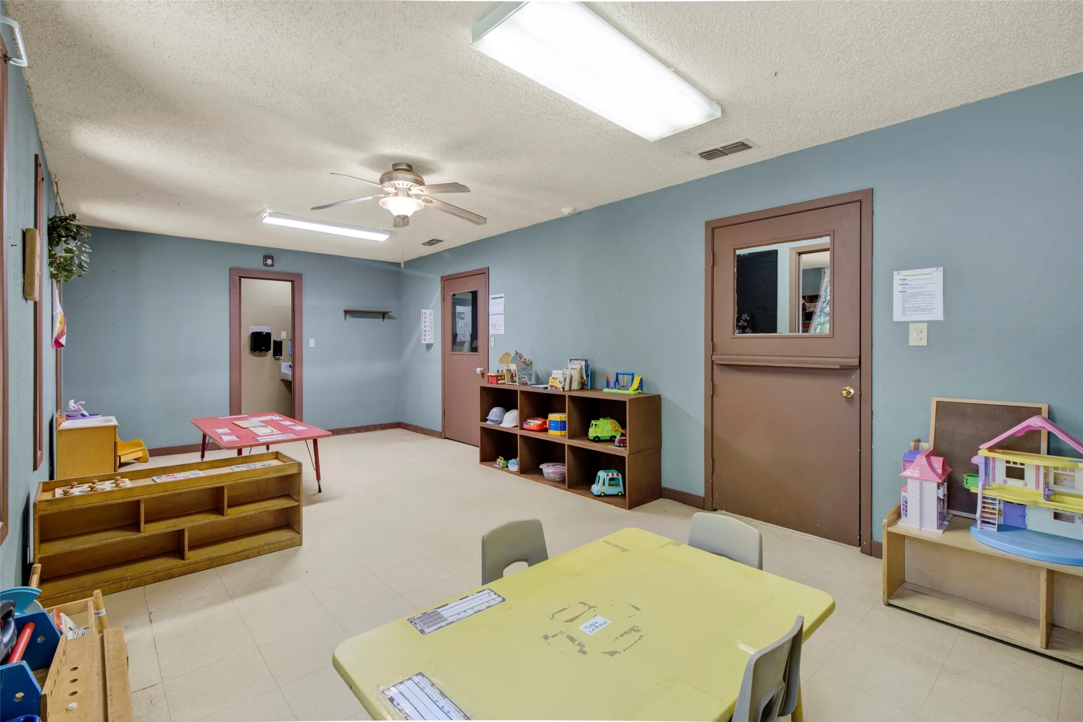 Spacious room featuring light blue walls, tile-finish flooring, and multiple ceiling-mounted light fixtures
