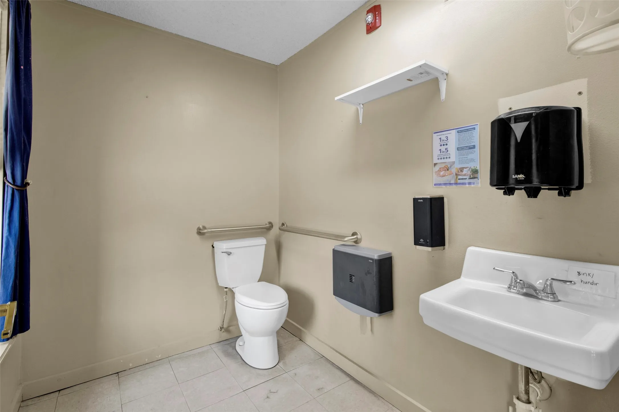Restroom featuring a white wall-mounted sink, a two-piece toilet, and multiple grab bars