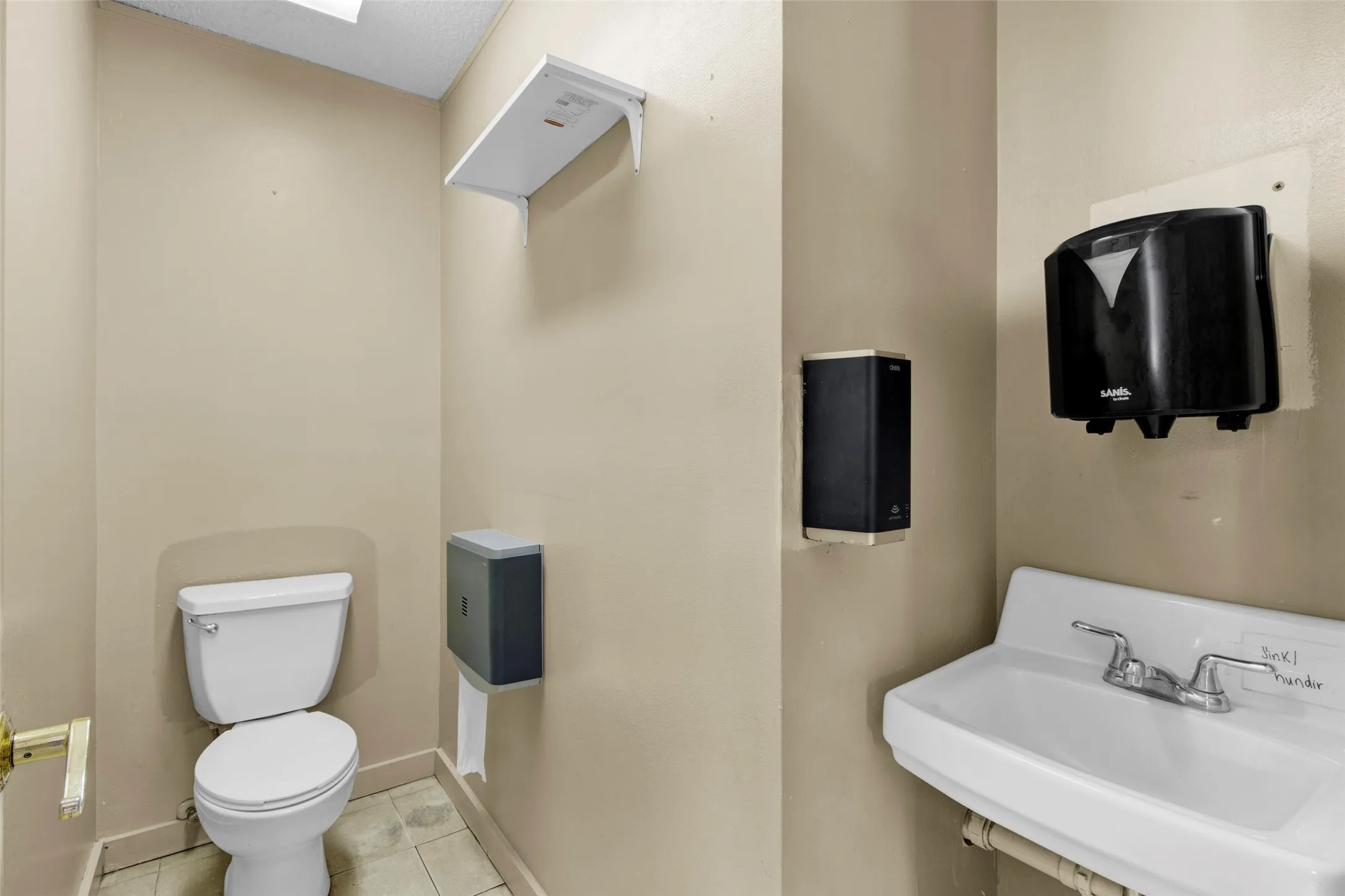 Functional restroom featuring a white toilet, wall-mounted sink, and light-toned tile flooring