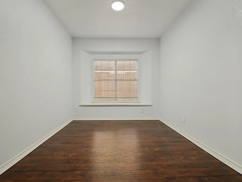 Room featuring wood-finish flooring, white baseboards, a bay window with blinds, and an overhead flush-mount light fixture