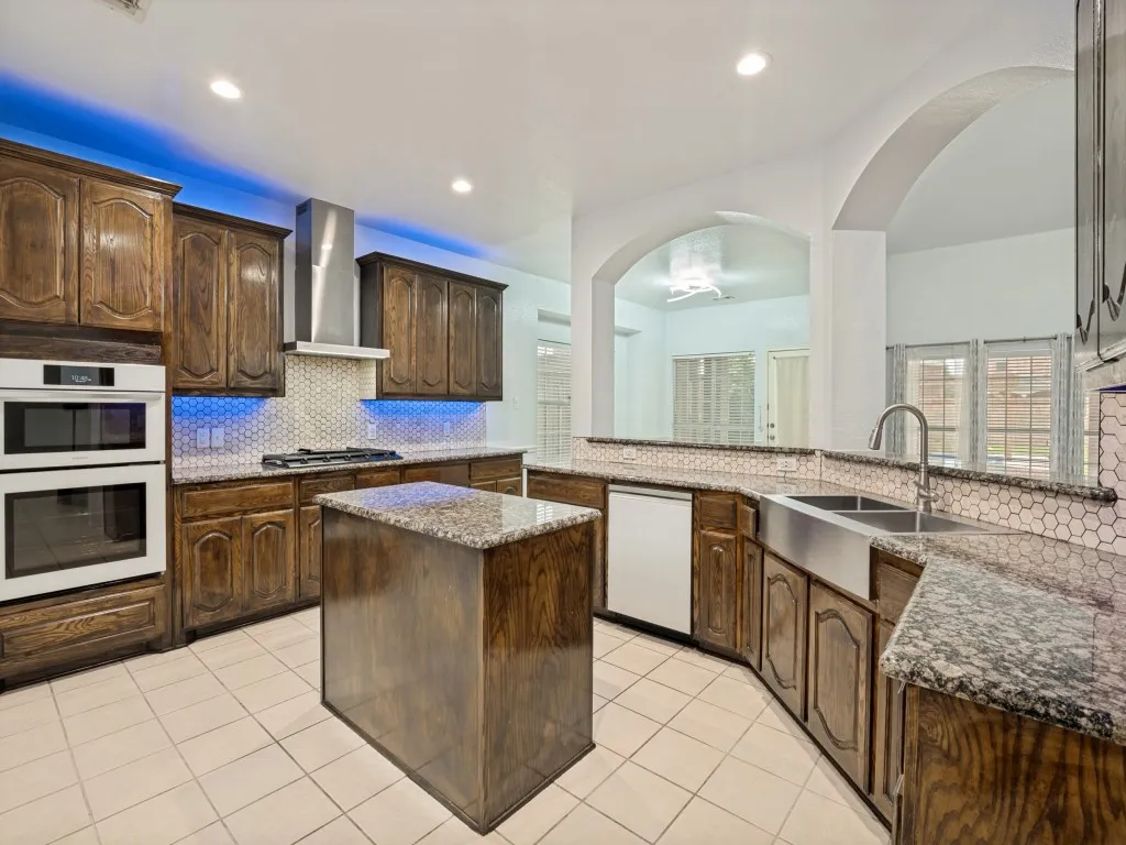 Spacious kitchen featuring warm wood cabinetry, granite countertops, an undermount double basin sink, stainless steel appliances, and tile flooring