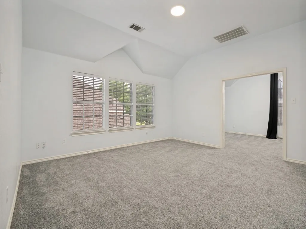 Spacious room featuring vaulted ceilings, light gray carpeting, and white baseboards