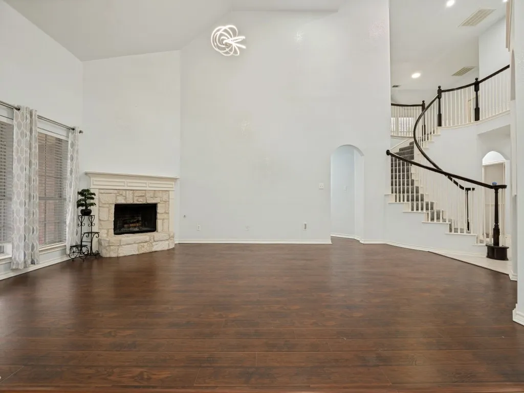 Spacious living area featuring high vaulted ceilings, rich wood-finish flooring, and a stone-clad fireplace with a decorative mantel
