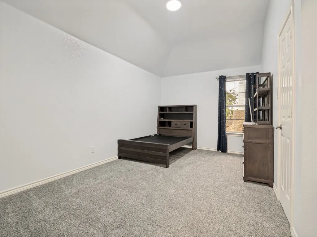 Vaulted ceiling room featuring light gray carpeting, neutral wall paint, and a window with dark curtains