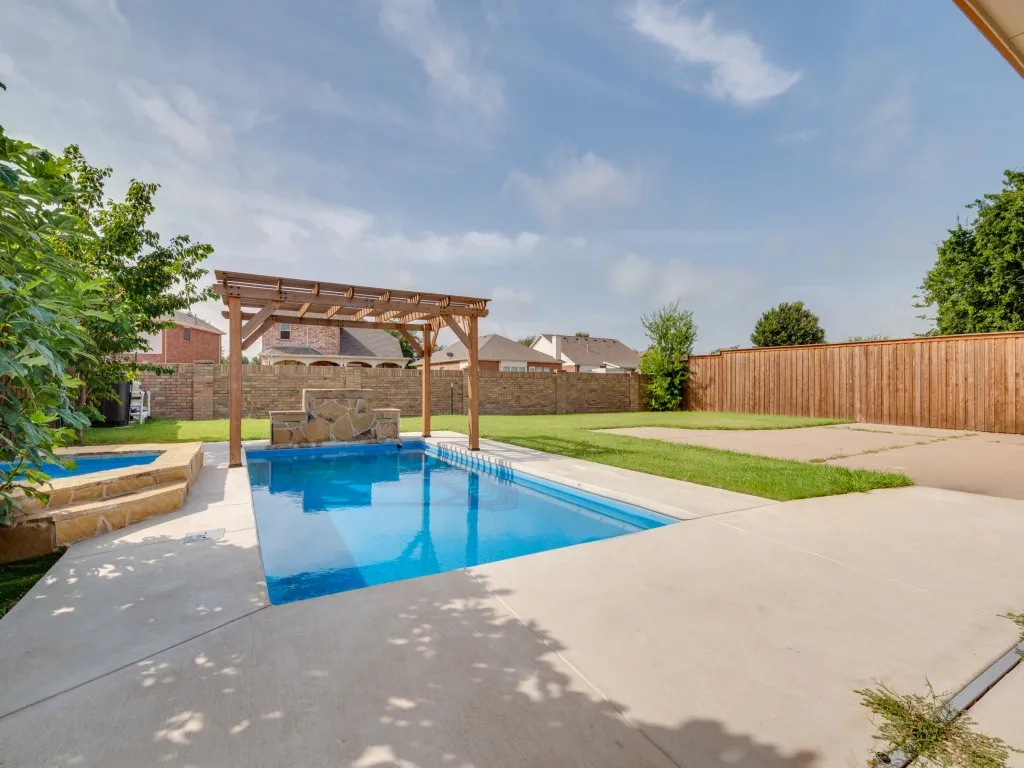 Backyard oasis featuring a rectangular swimming pool, an attached spa with stone steps, and a wooden pergola over a stone-clad water feature