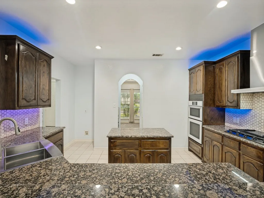 Kitchen featuring dark wood cabinetry, speckled granite countertops, and a hexagonal tile backsplash