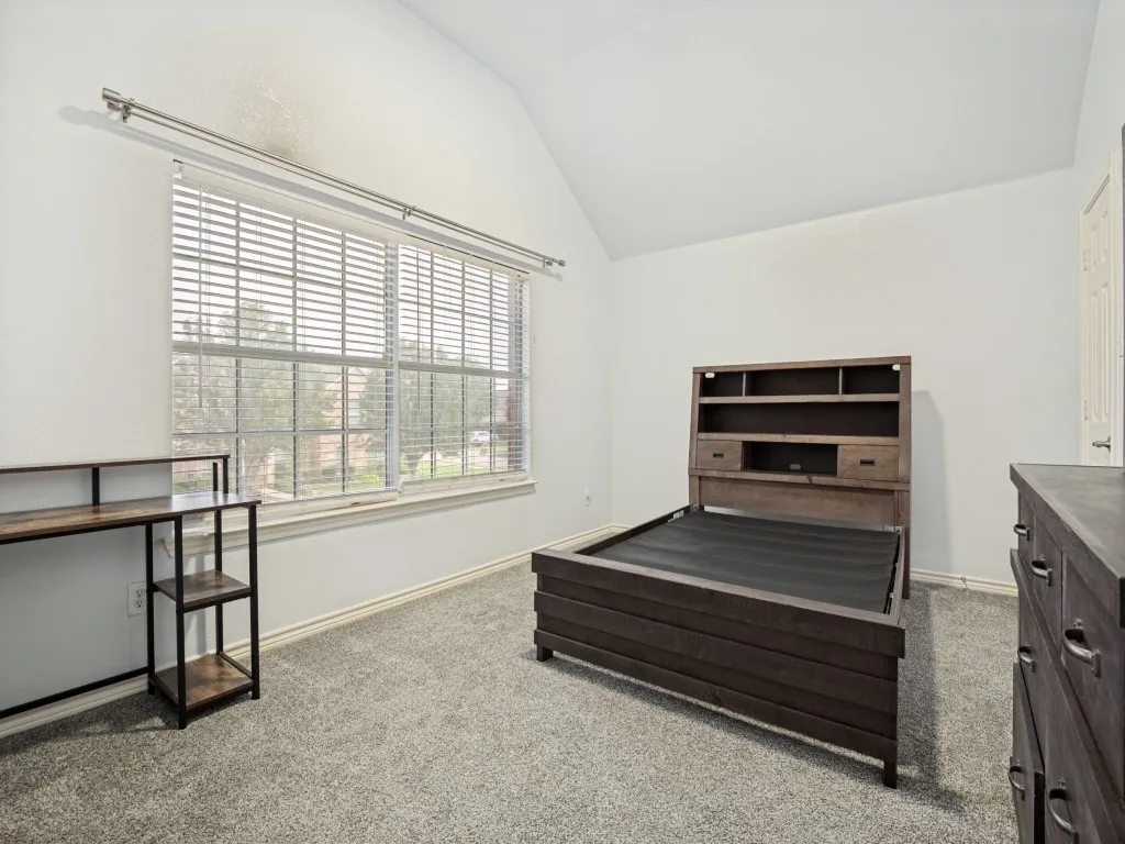 Vaulted ceiling room featuring light gray carpeting and a large window with blinds