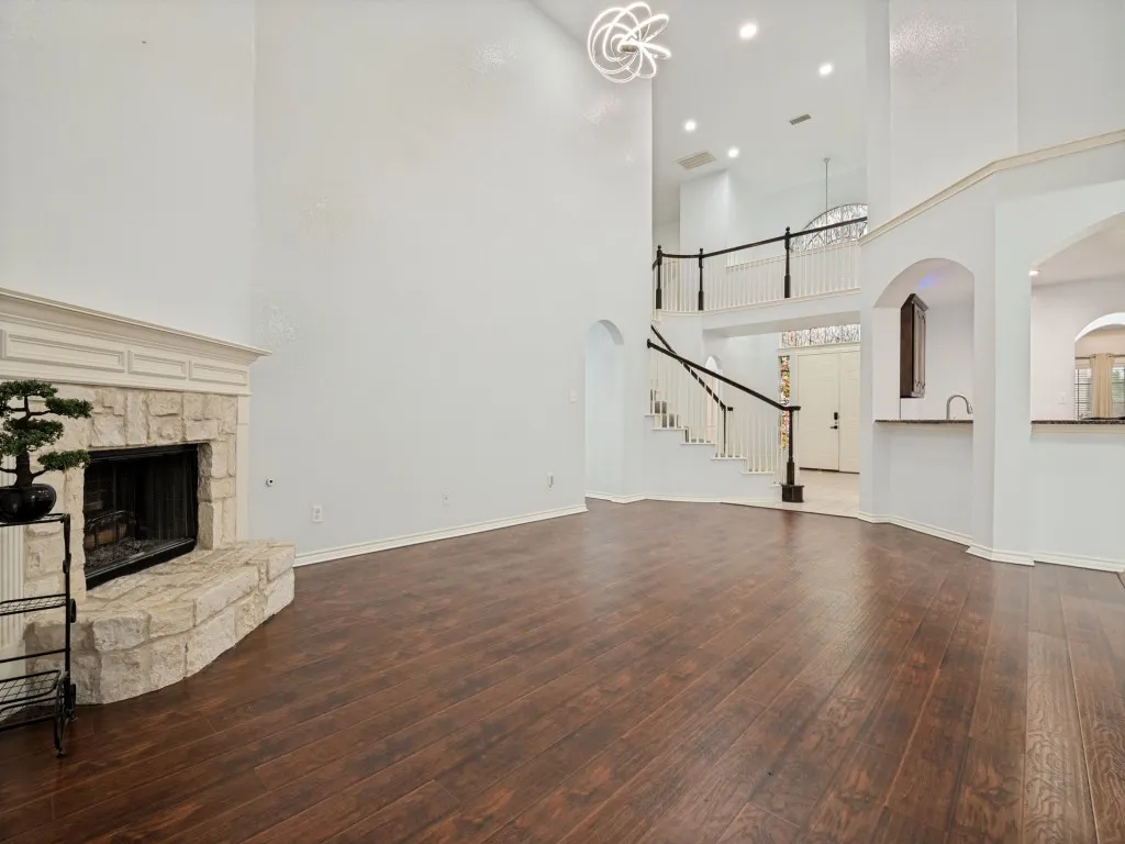 Two-story living area featuring dark wood-finish flooring, a stone fireplace with a white mantel, and a prominent staircase with dark railings and white balusters