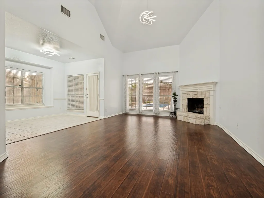 Spacious living area featuring high vaulted ceilings, rich wood-finish flooring, and a corner fireplace with a stone surround