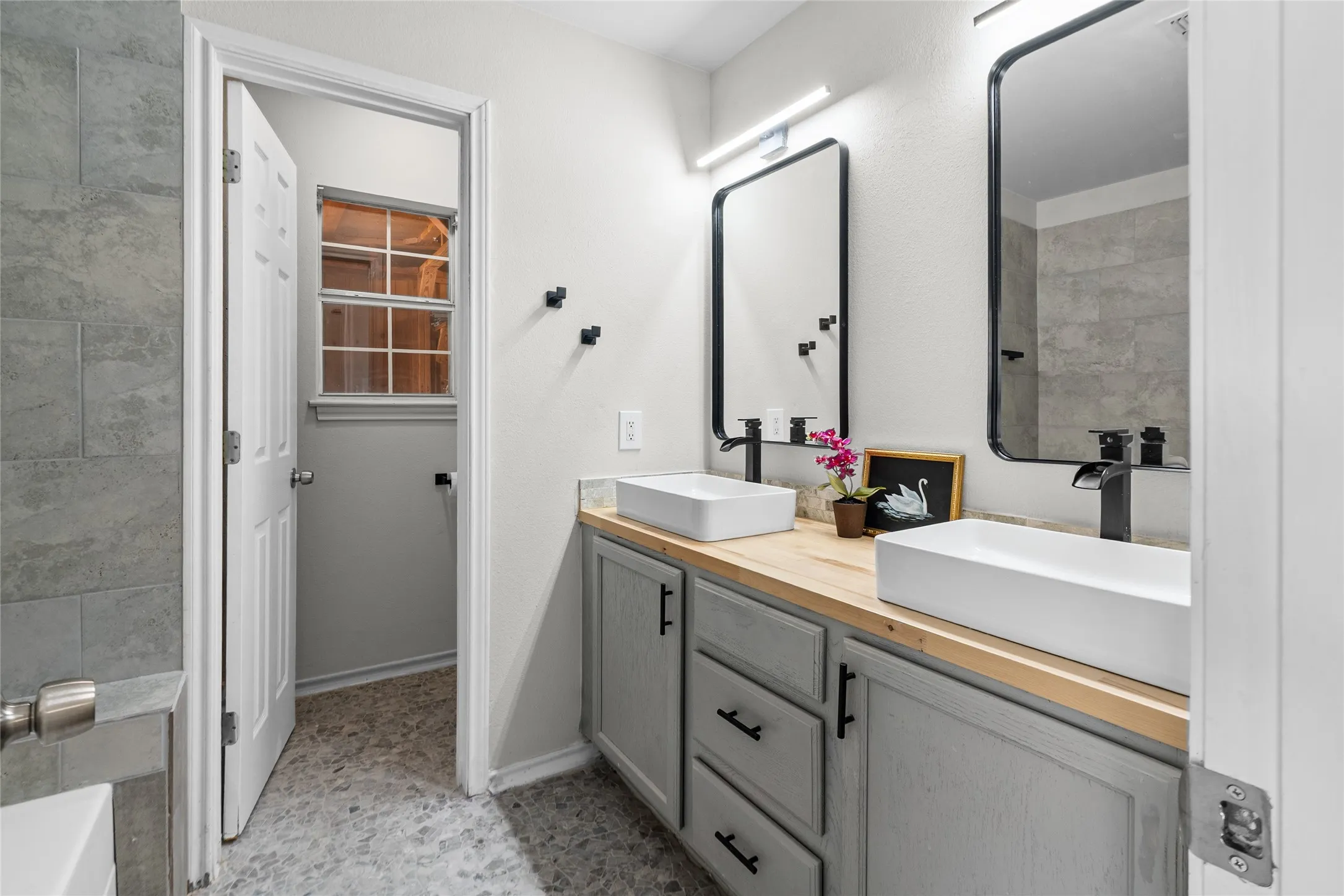 Primary Bathroom with Dual vessel sinks set atop a wood-finish vanity with gray cabinetry and matte black hardware