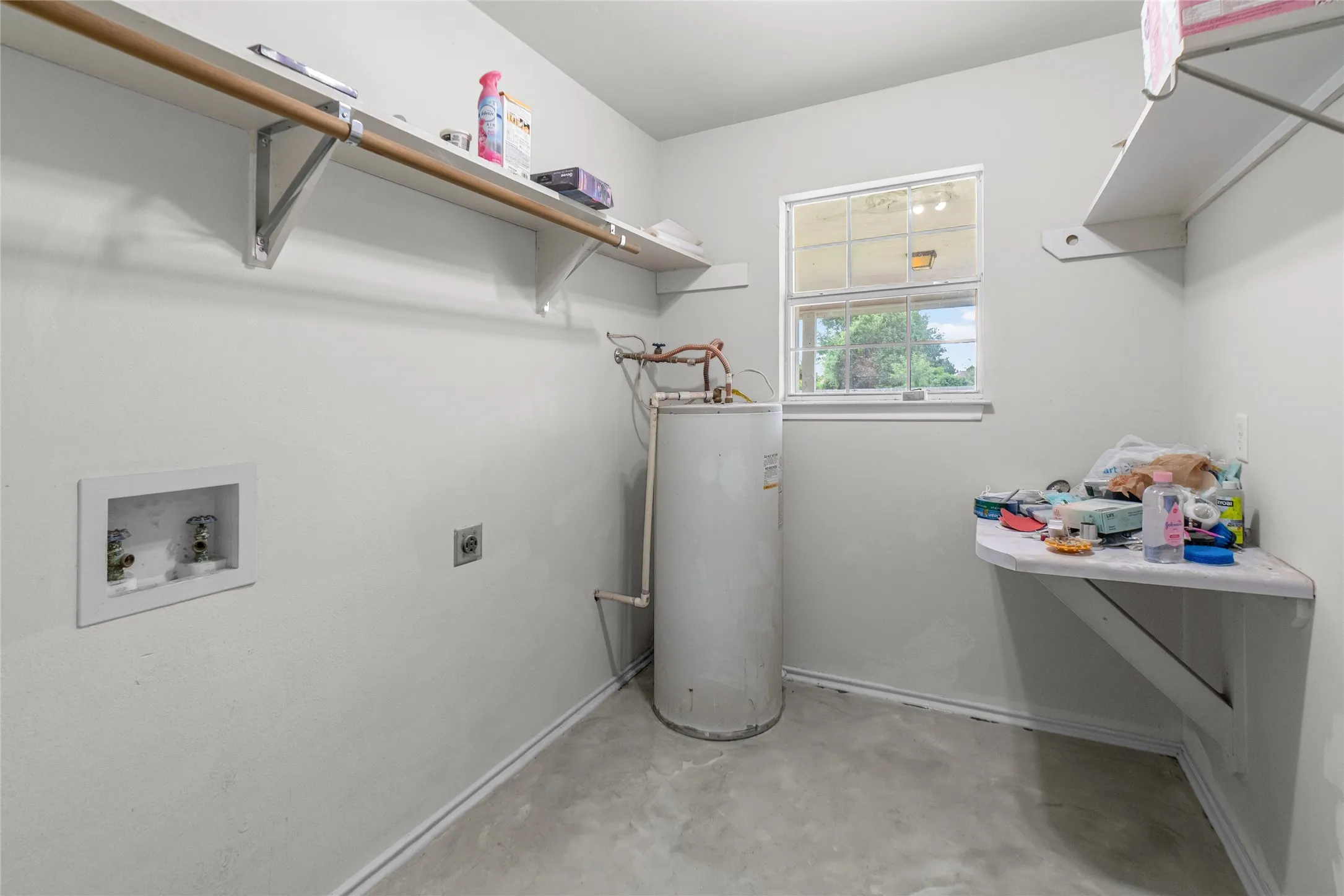 Utility room featuring a window, water heater, and concrete flooring