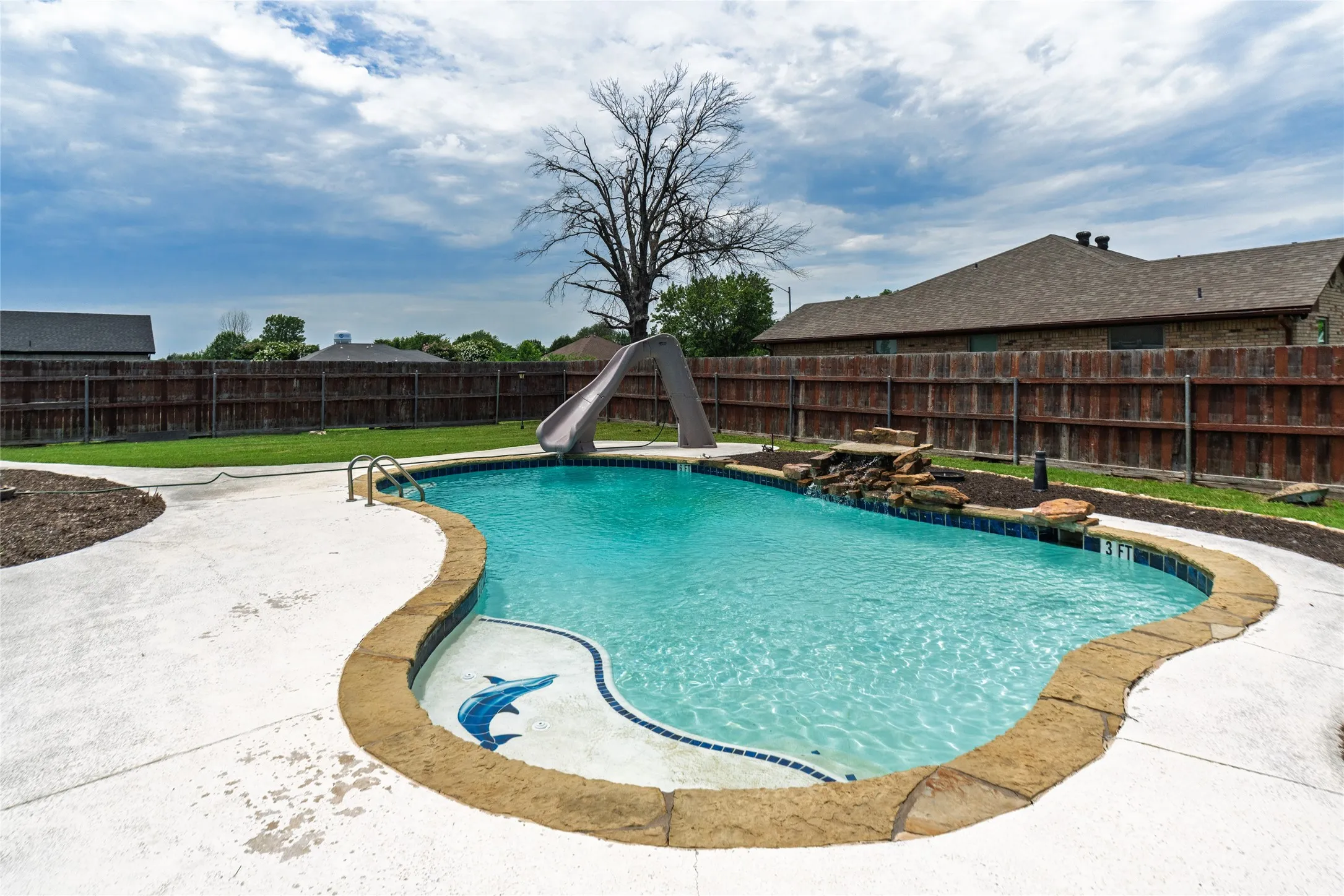 Curvilinear swimming pool featuring a built-in slide, stone coping, and a waterfall rock feature