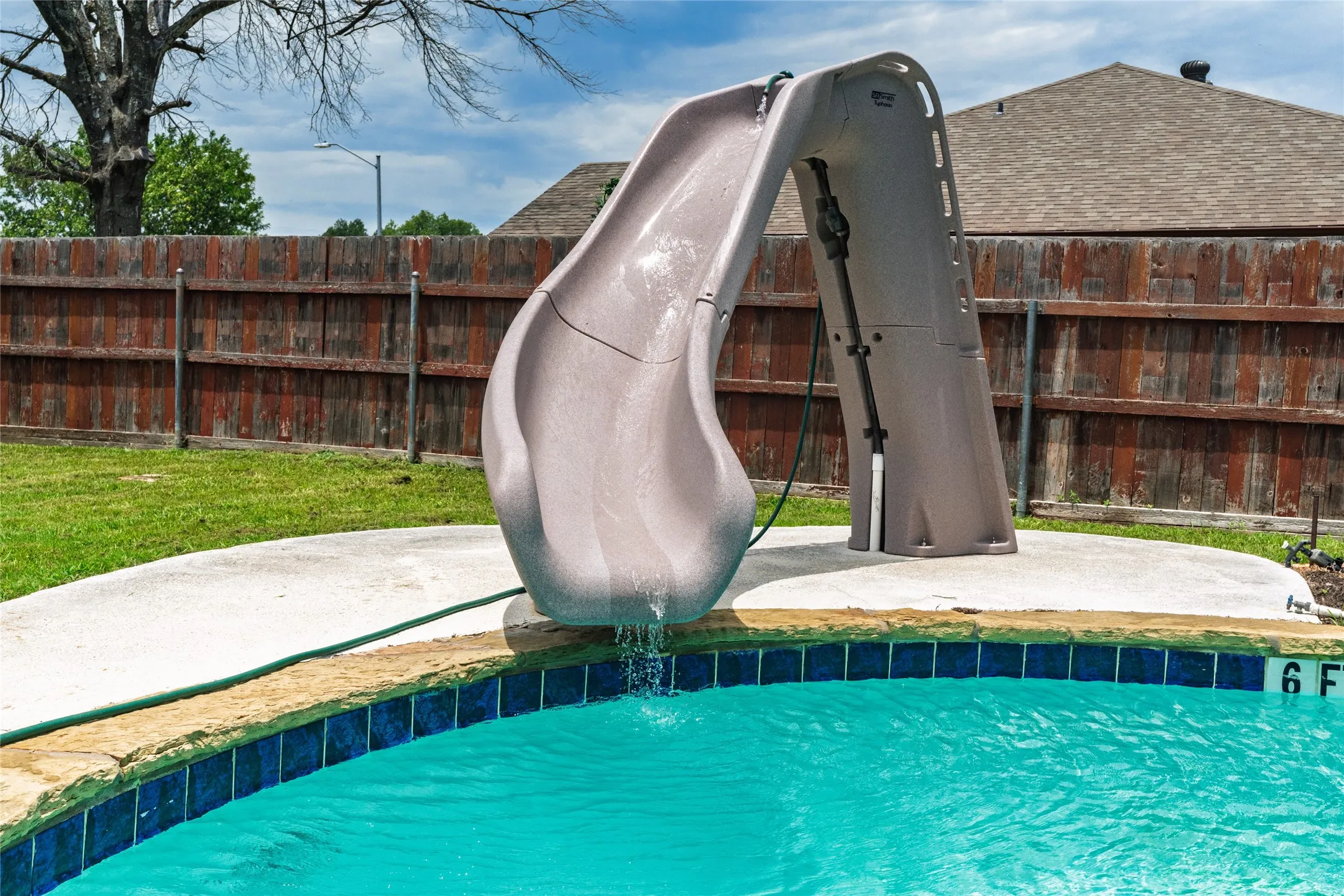 Swimming pool featuring a gray slide, blue waterline tiles, stone coping, and concrete decking