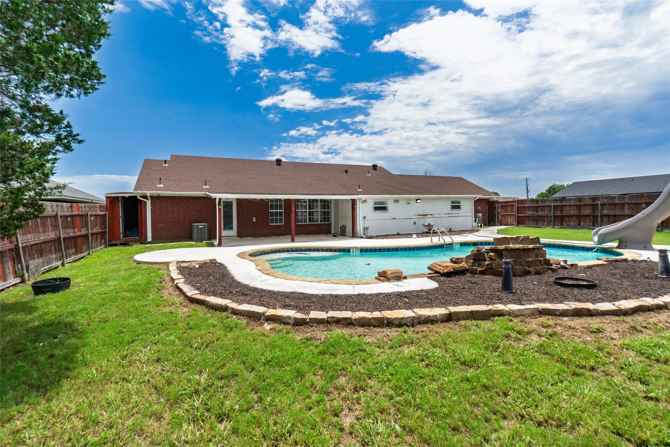 Backyard with a freeform swimming pool, concrete patio surround, and a decorative rock water feature