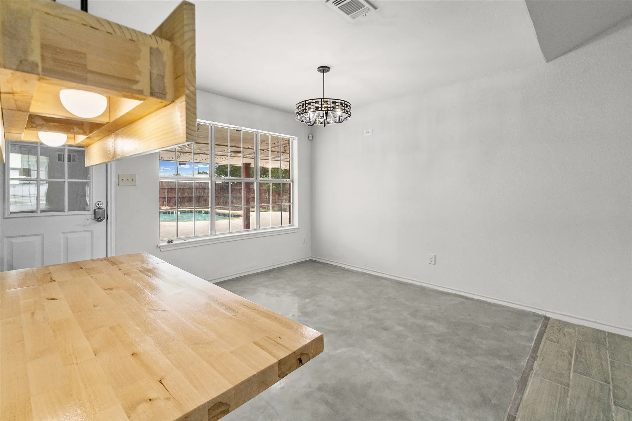 Light wood block countertop with an integrated custom light fixture, an ornamental chandelier, and large windows with backyard pool visibility