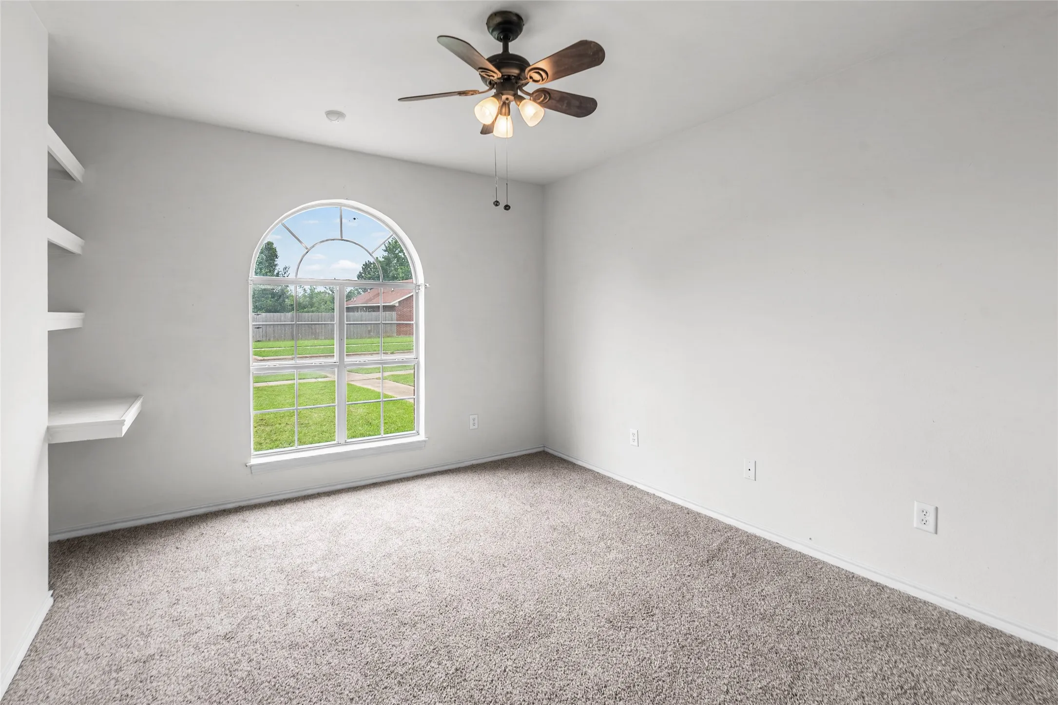 Bedroom featuring an arched window, built-in shelving, carpet flooring, a ceiling fan, and white walls