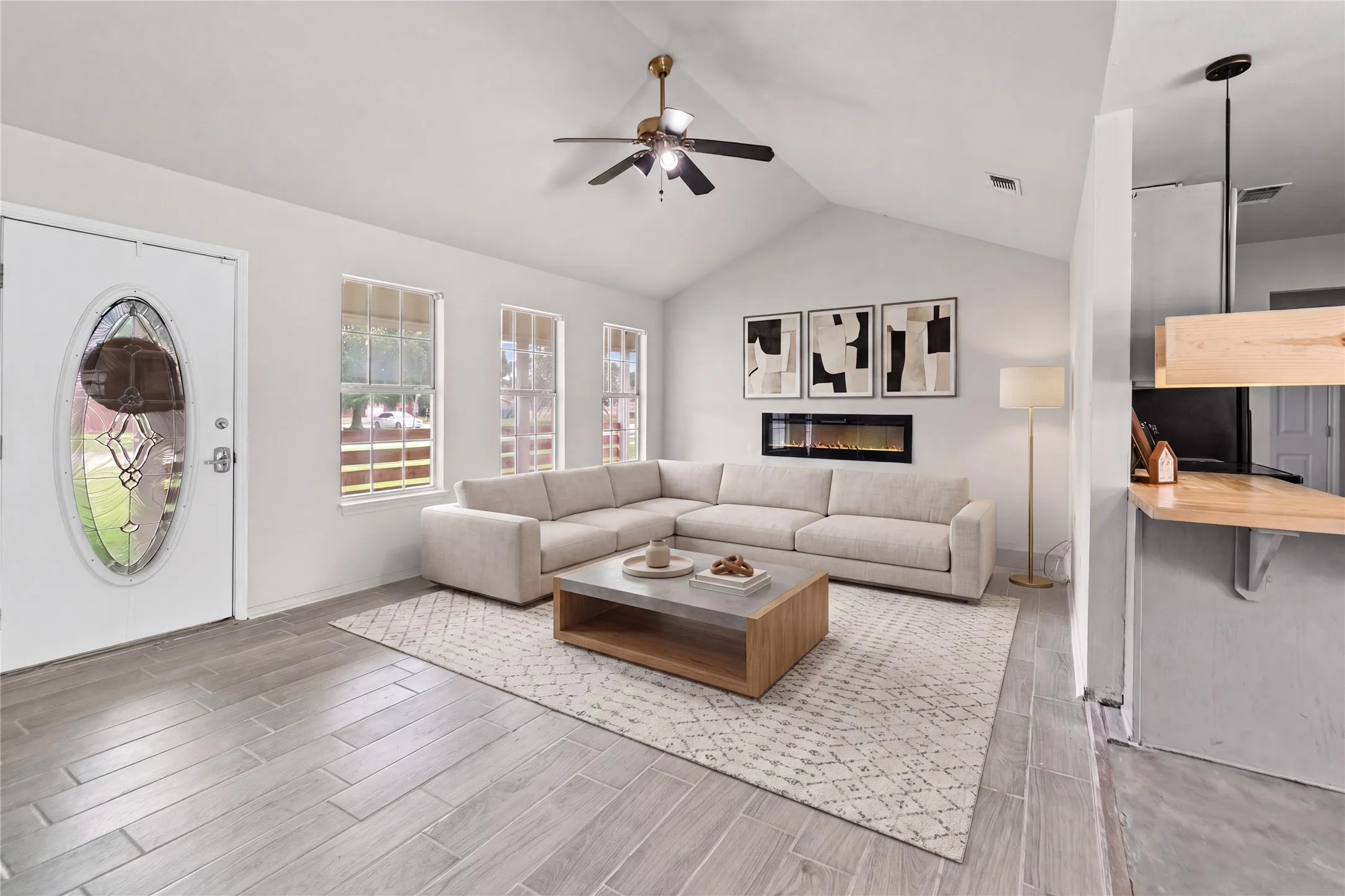 Virtually Staged -Spacious living area featuring light wood-finish flooring, vaulted ceilings, and an electric fireplace