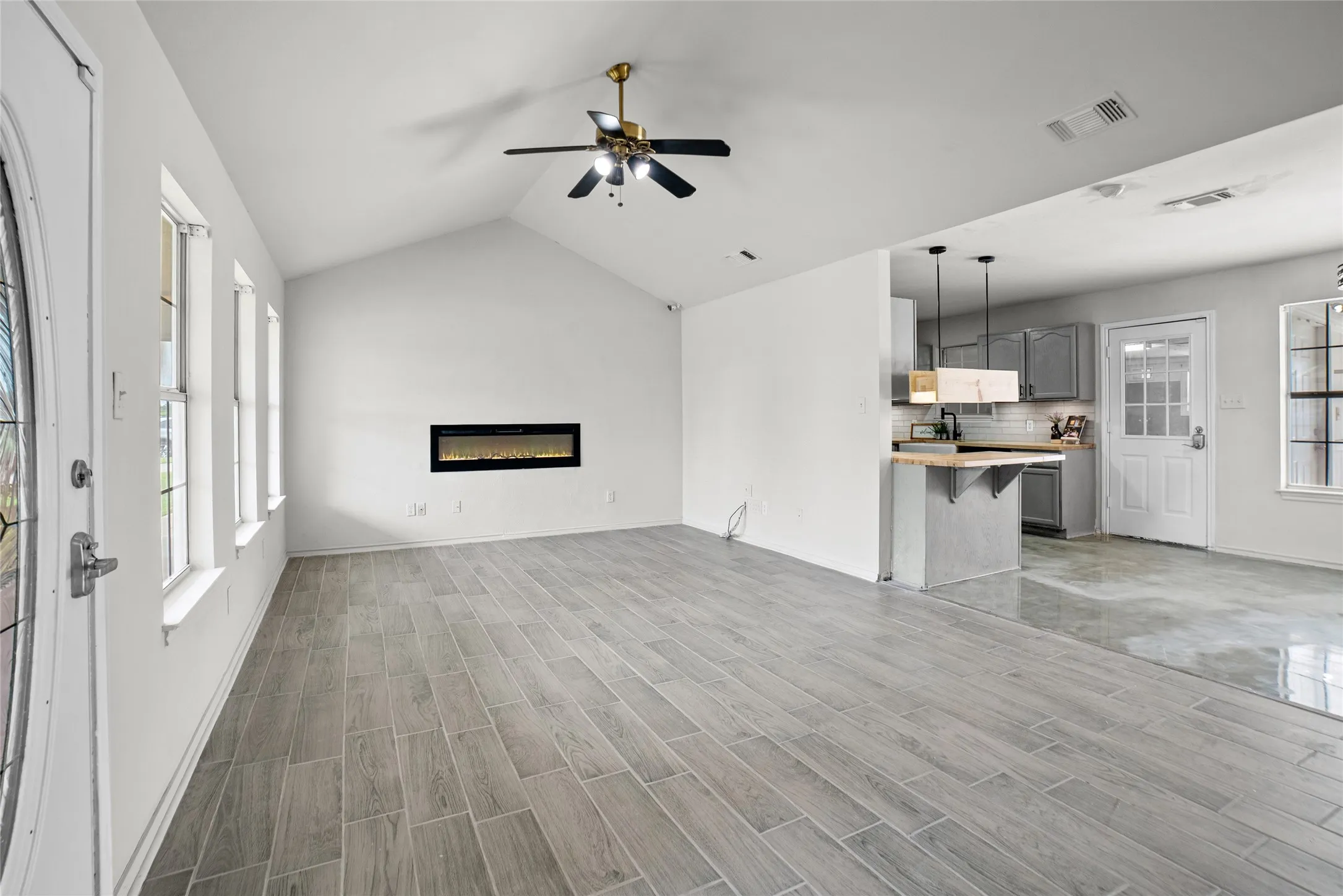Bright living area featuring vaulted ceilings, wood-finish tile flooring, an elongated electric fireplace, and three large windows