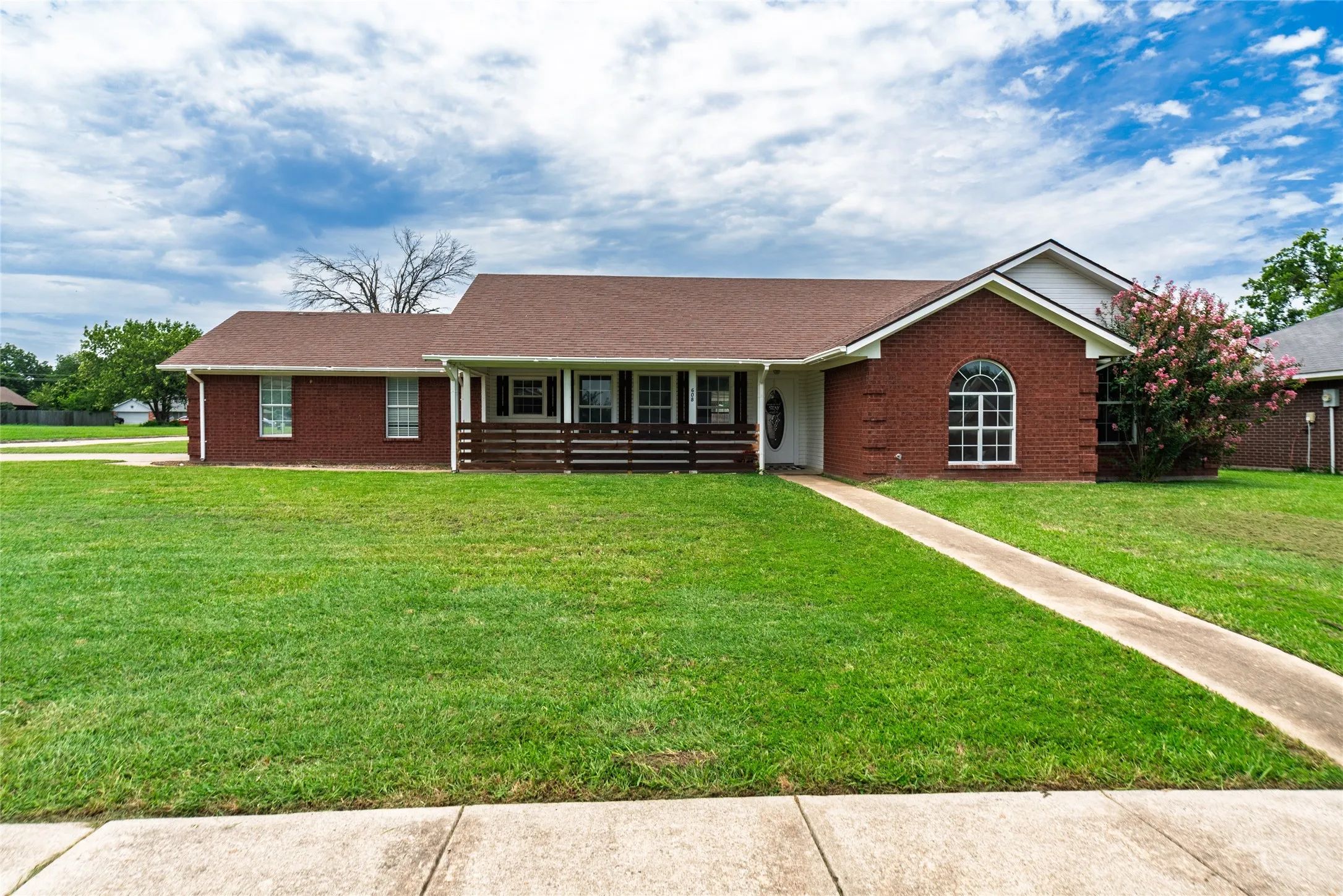 Brick facade residence featuring a covered front porch with horizontal railings, a prominent arched window, and a concrete walkway