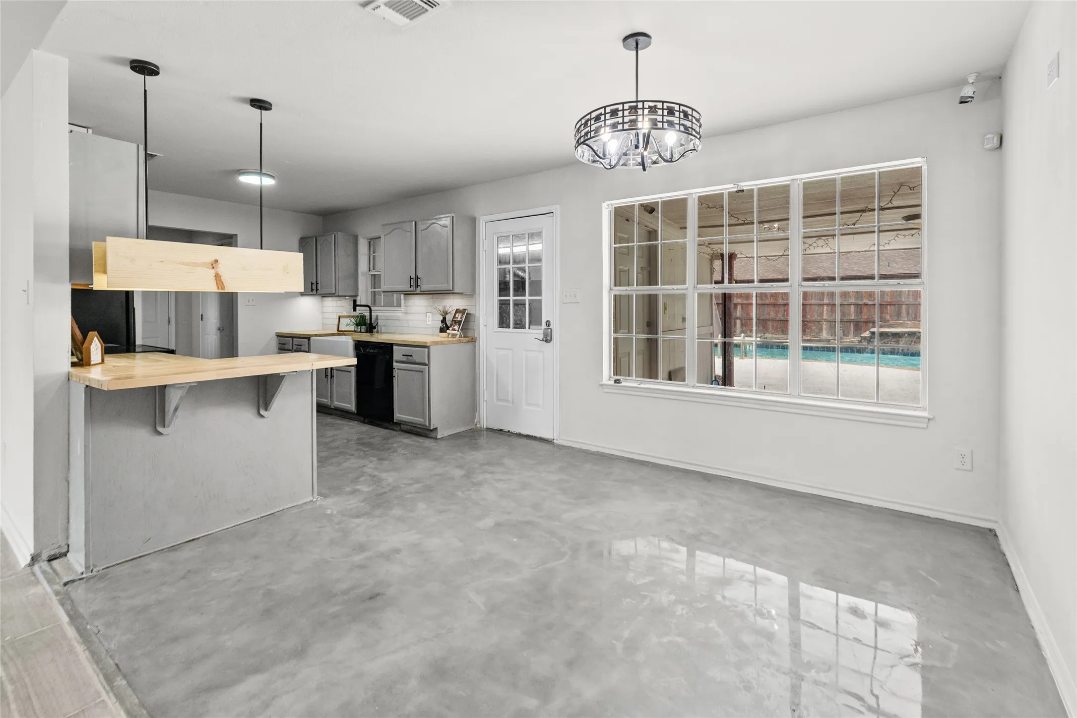 Open-concept living area with polished concrete flooring, a modern chandelier, and a large multi-pane window providing a clear view of the outdoor pool